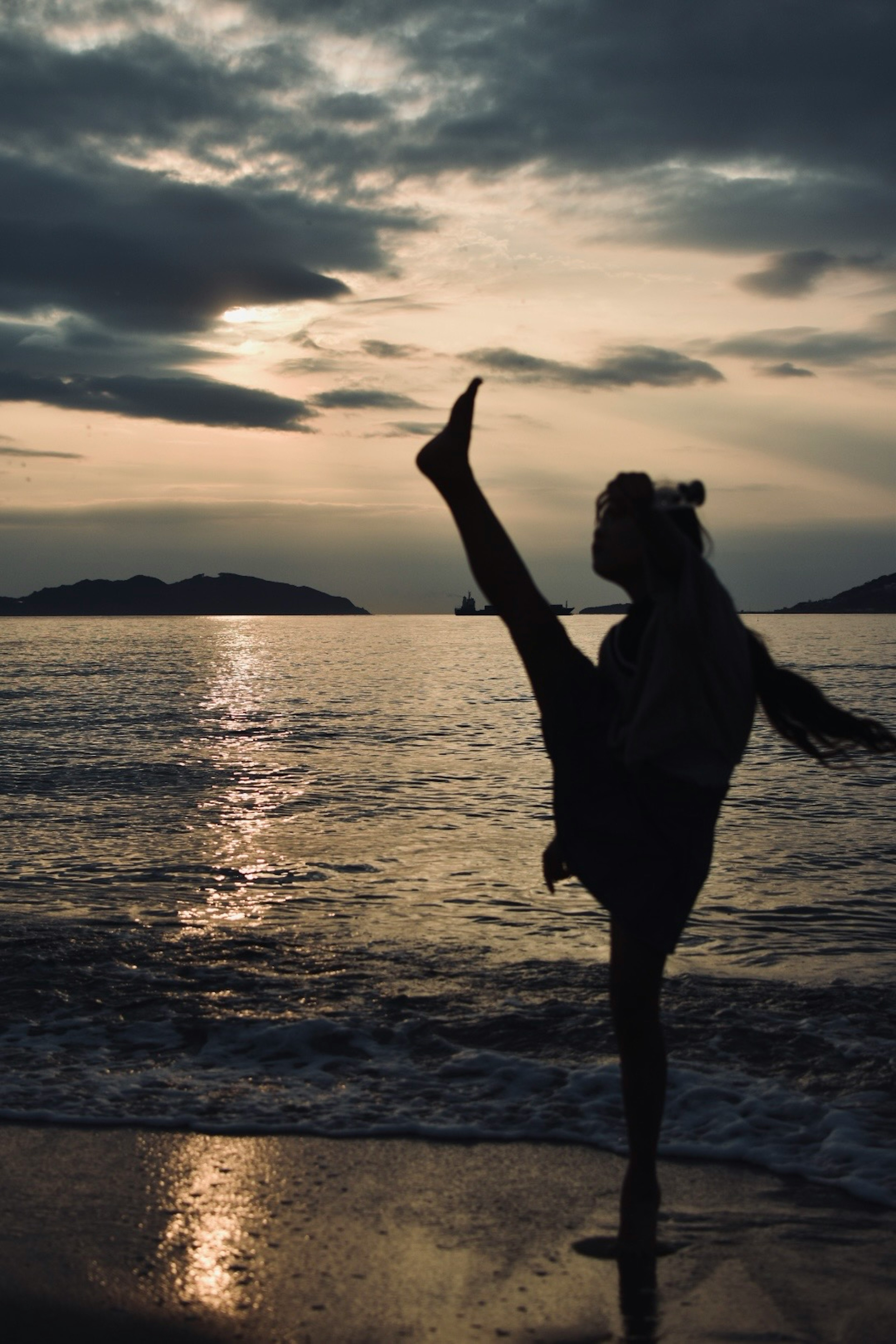 Silhouette d'une femme levant une jambe au coucher du soleil sur la plage