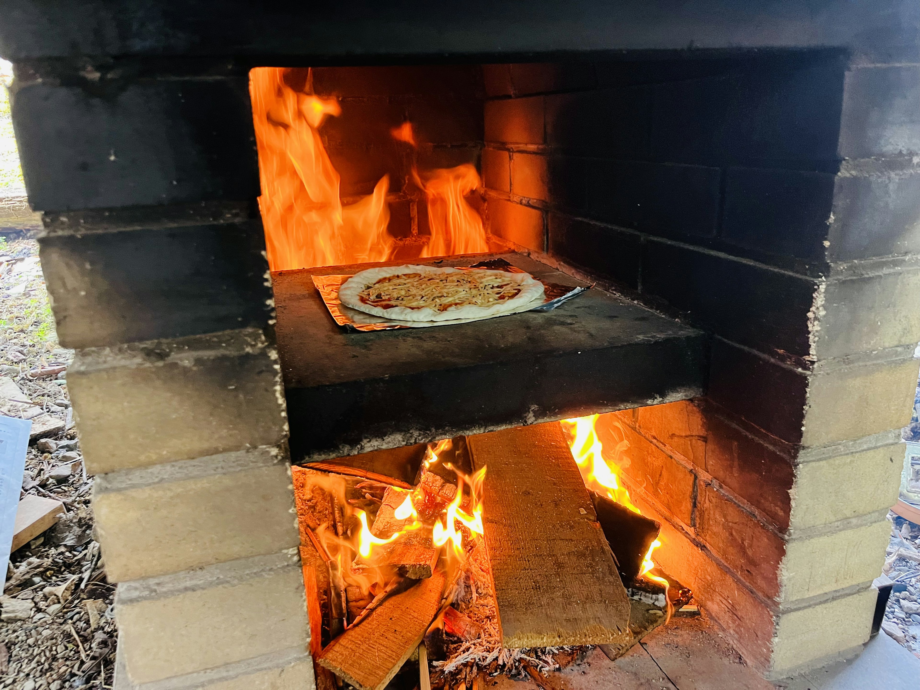 Pizza yang dimasak di oven bata dengan api terlihat