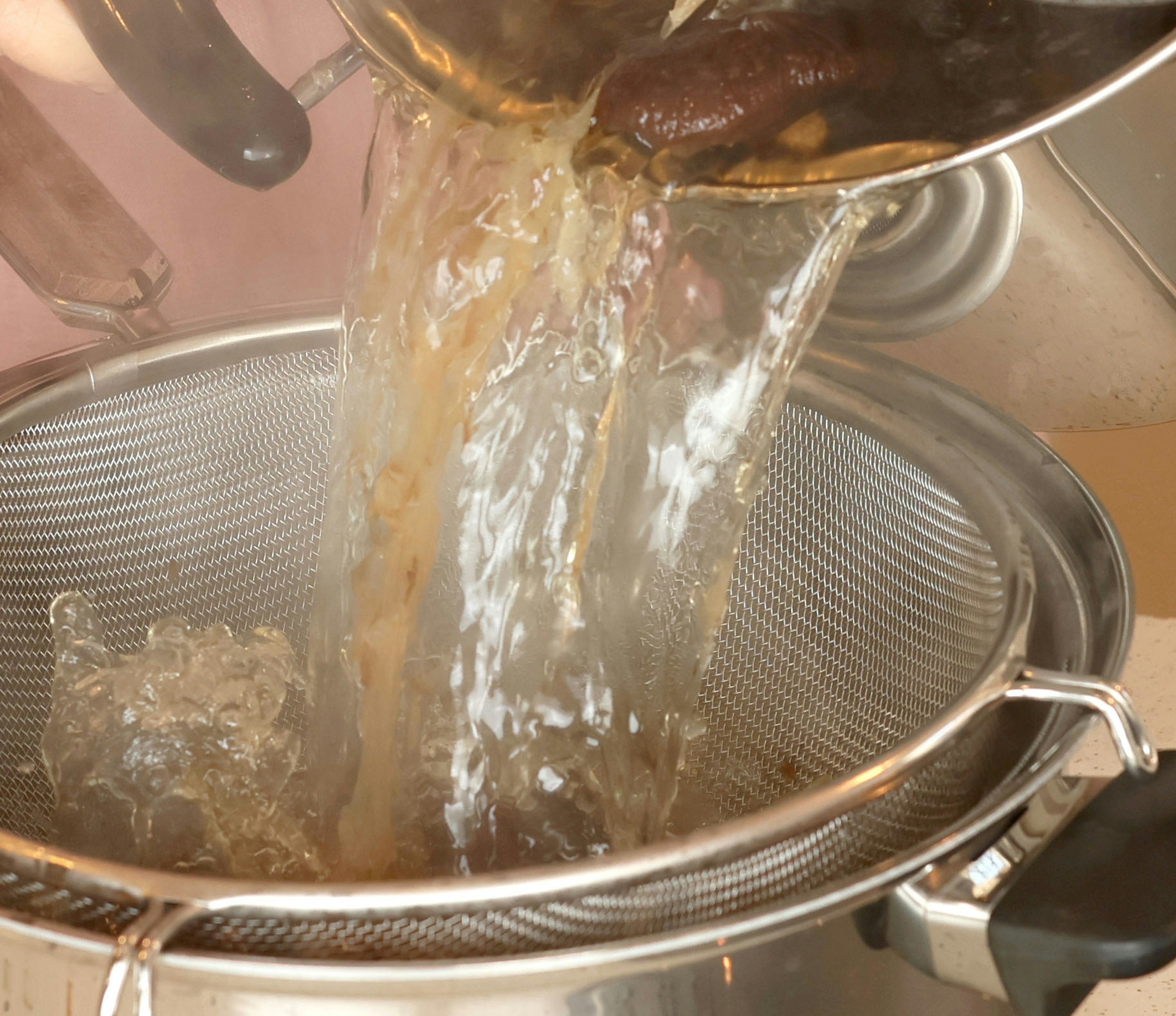 Hot liquid being poured from pot into strainer