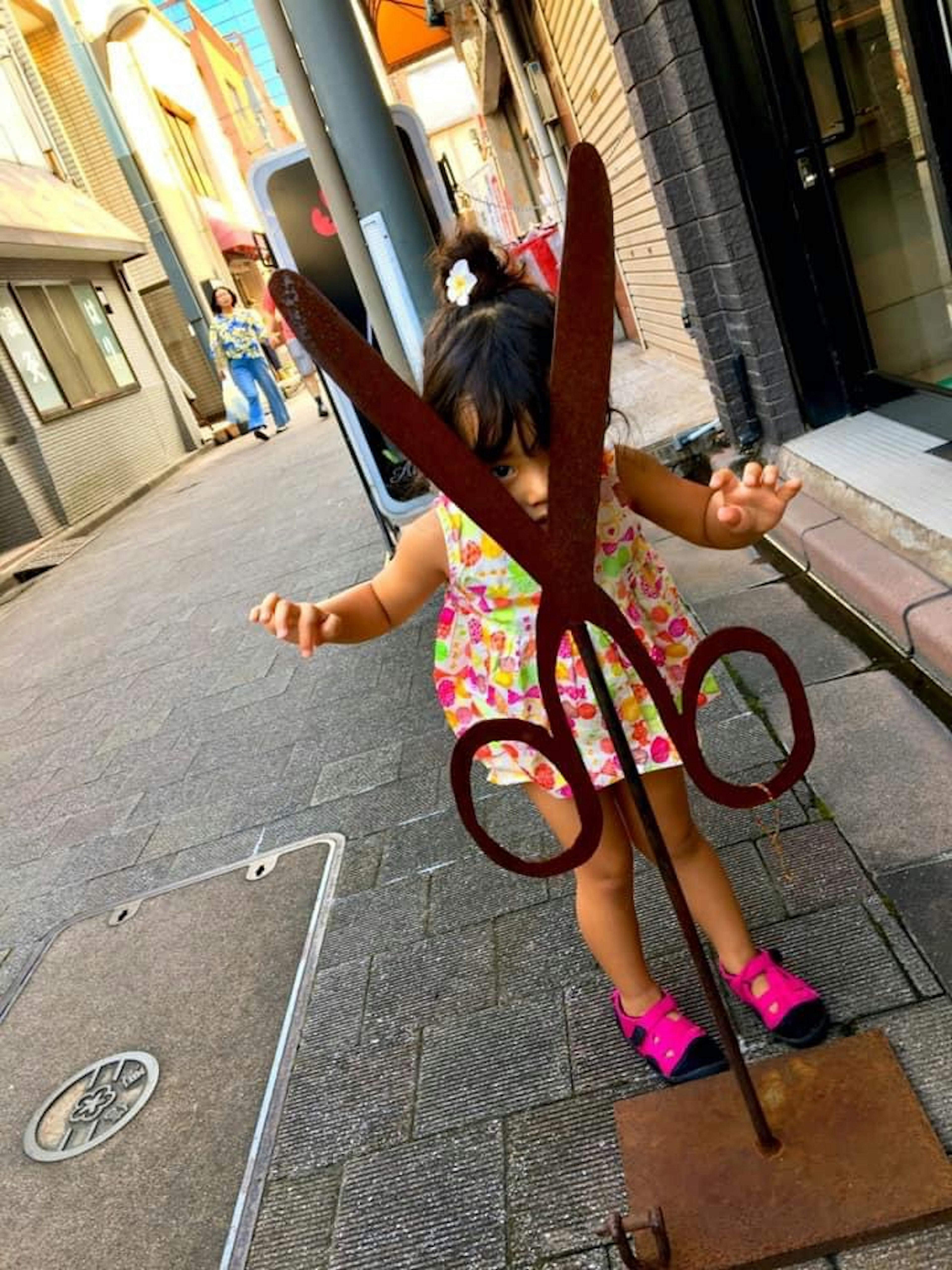 Niño jugando frente a una escultura de tijeras gigantes en una calle