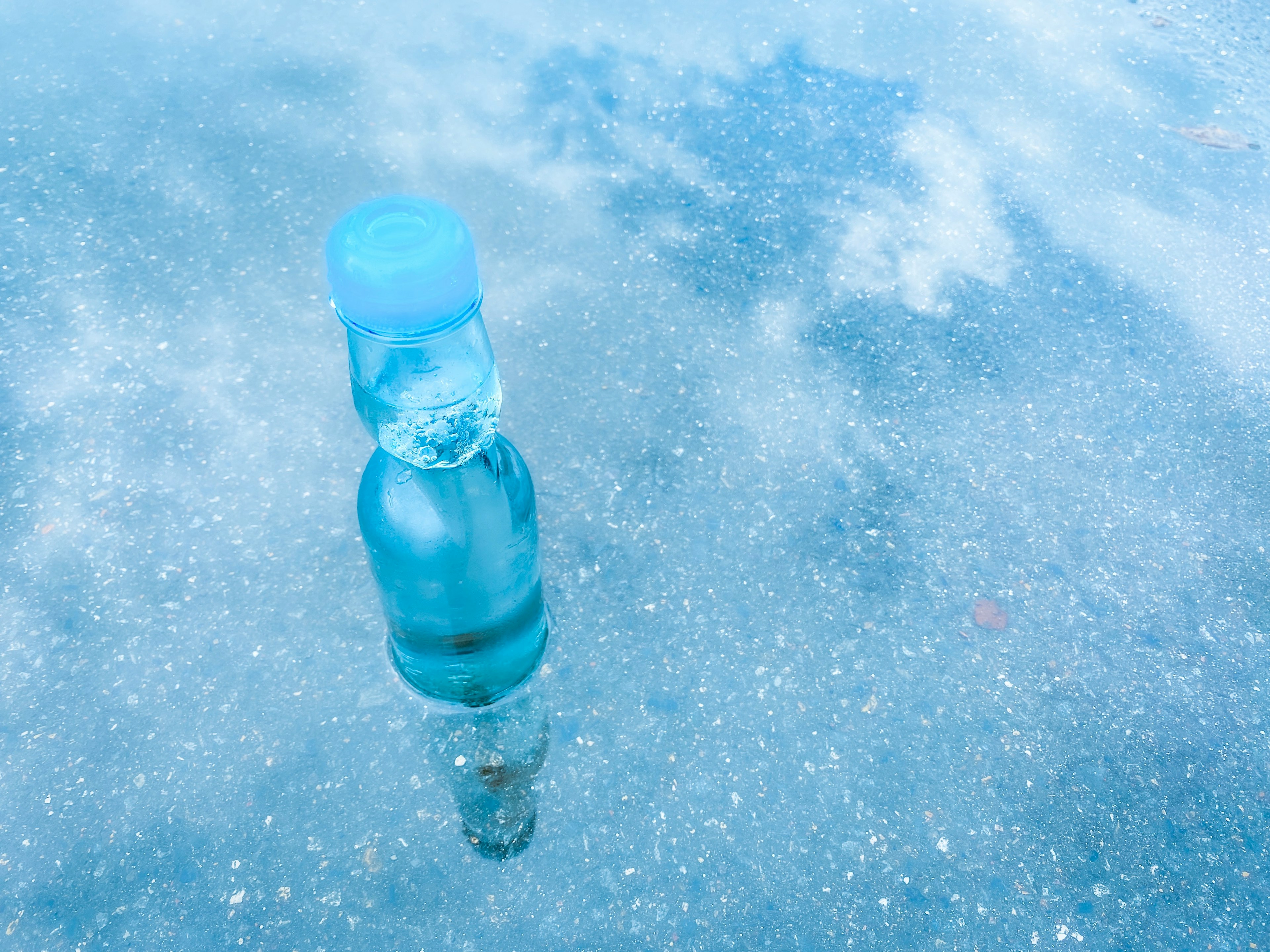 Blaue Flasche, die sich in einer Pfütze mit Himmelreflexionen spiegelt