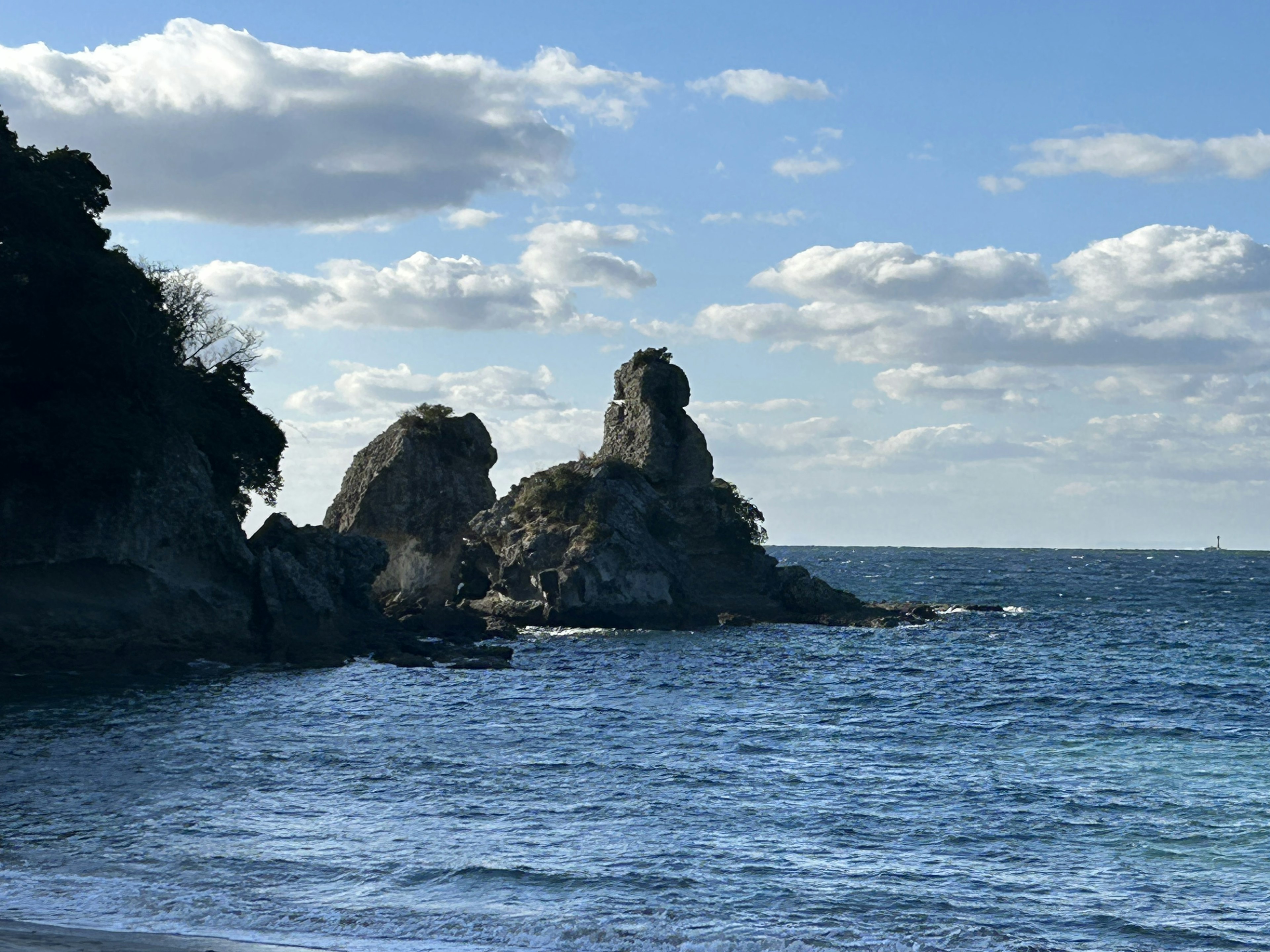 Rock formations rising from the blue sea under white clouds