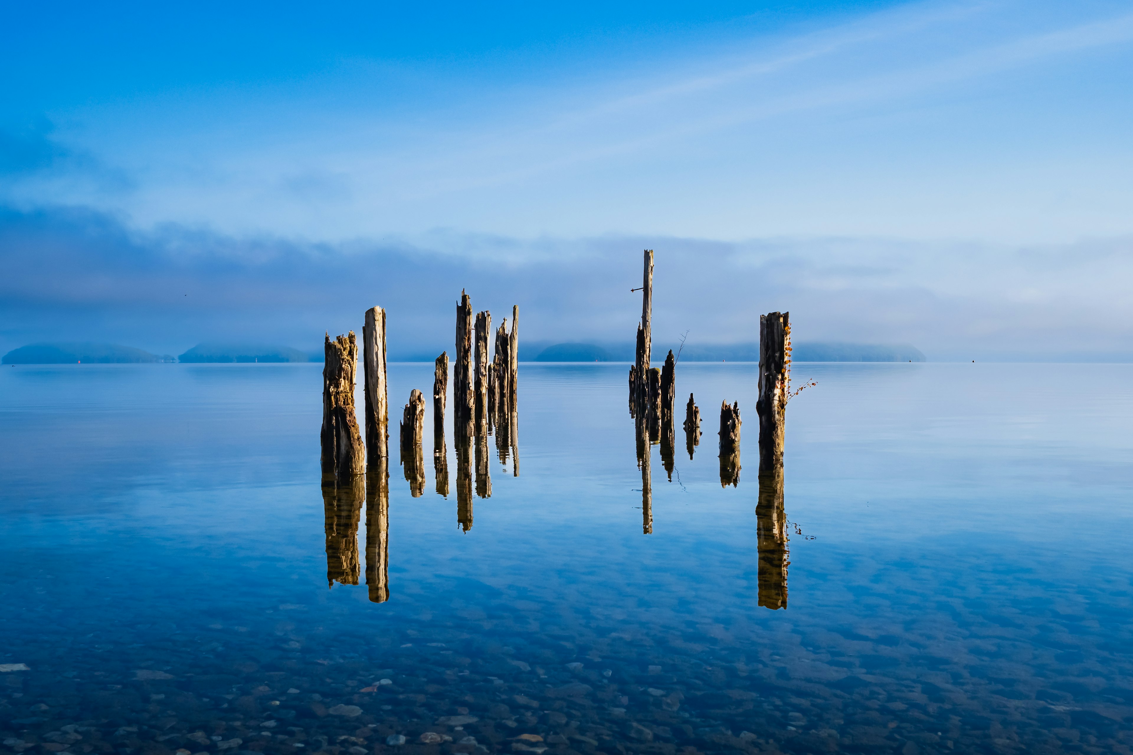 Anciens poteaux en bois reflétés dans l'eau calme sous un ciel bleu