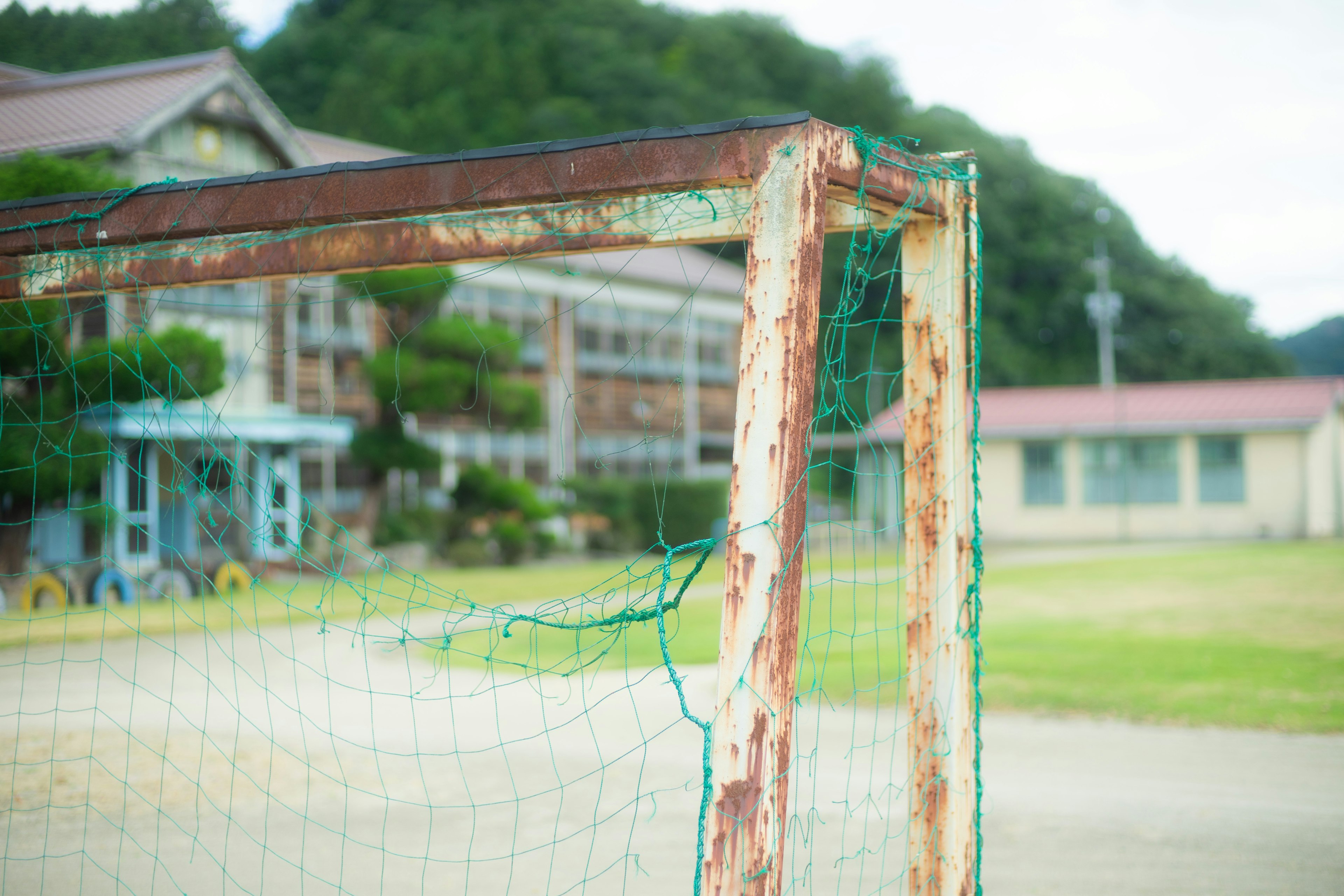 Portería de fútbol oxidada con un viejo edificio escolar al fondo