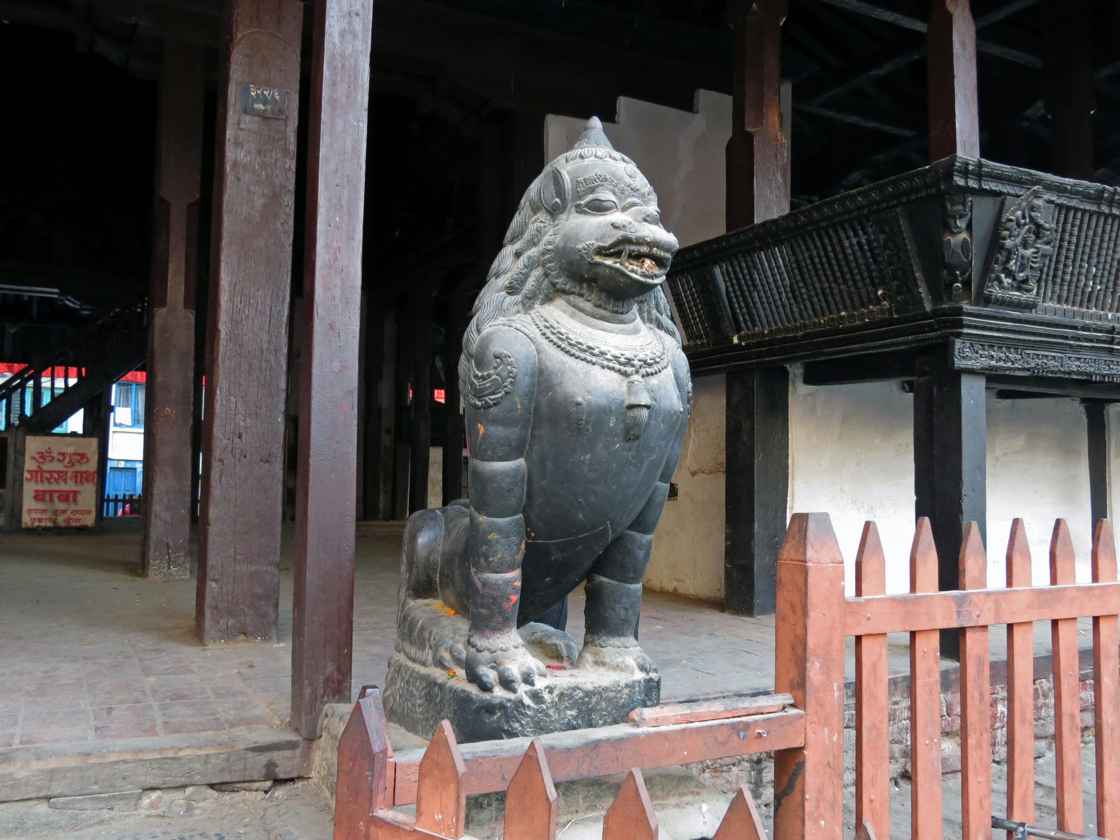 Steinstatue eines Löwen am Tempel-Eingang umgeben von einem Holzzaun mit traditionellem Gebäude im Hintergrund