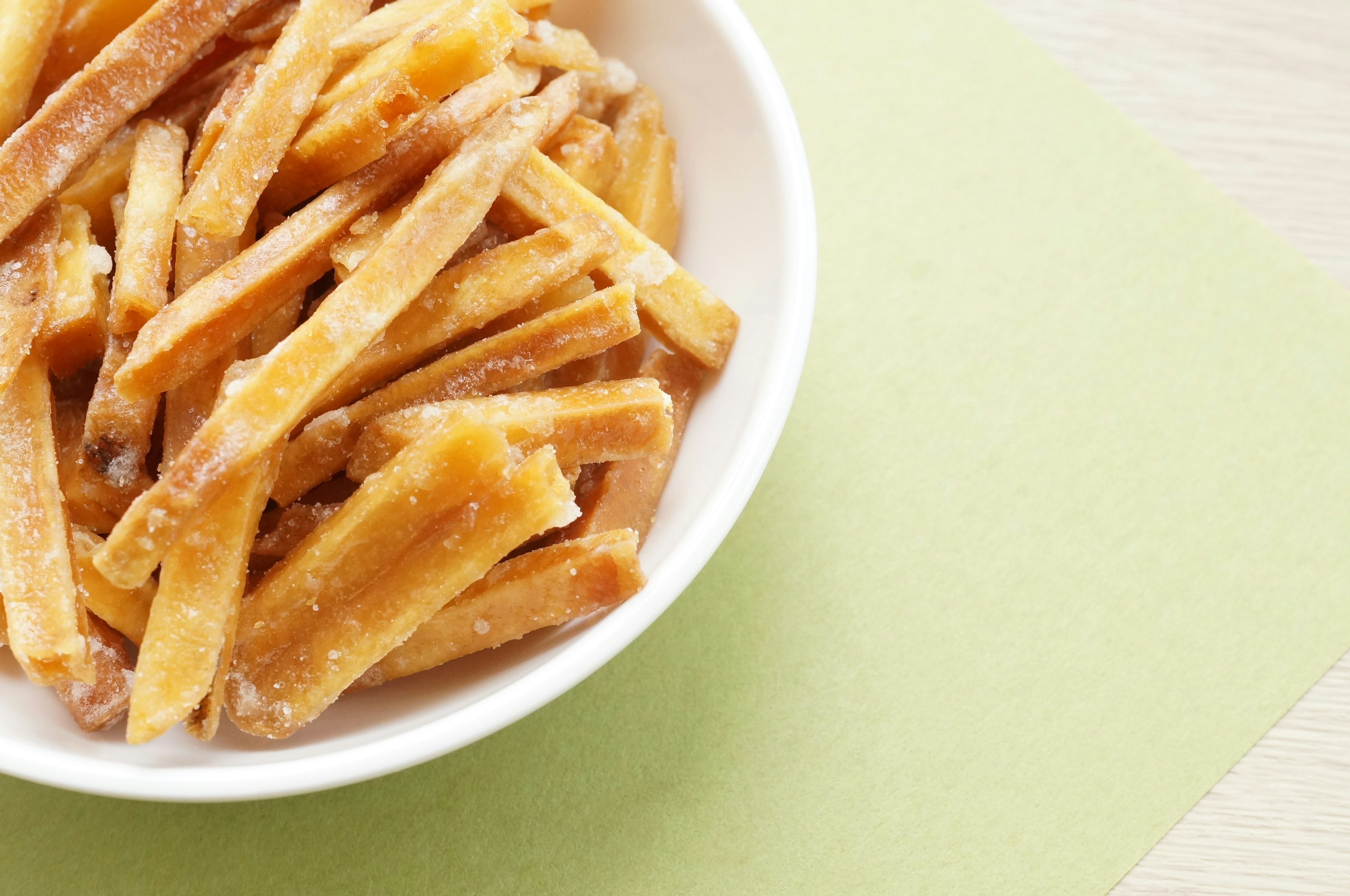 Sweet potato sticks in a white bowl on a green background