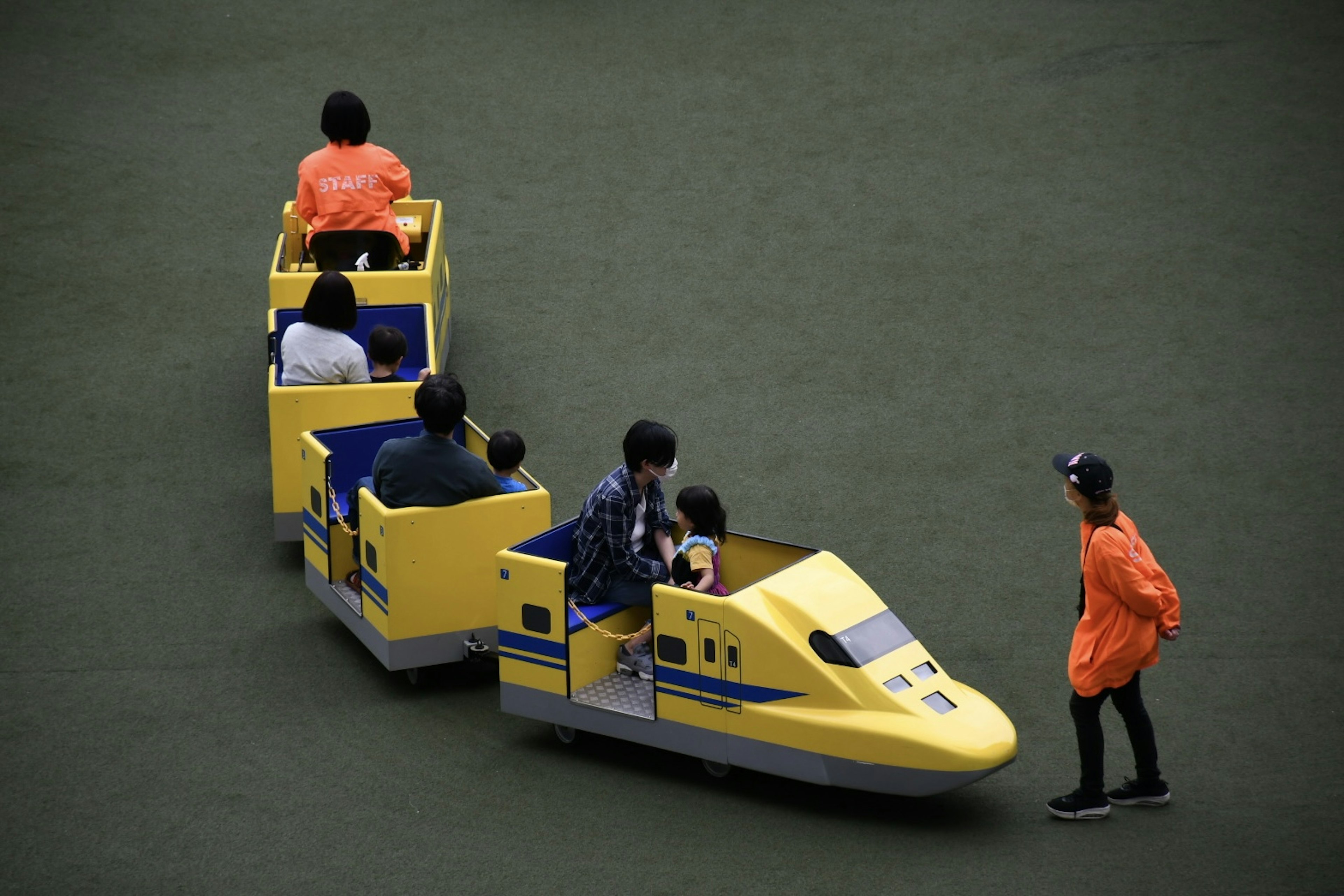 Niños montando en una atracción de tren amarillo con un miembro del personal vestido de naranja cerca