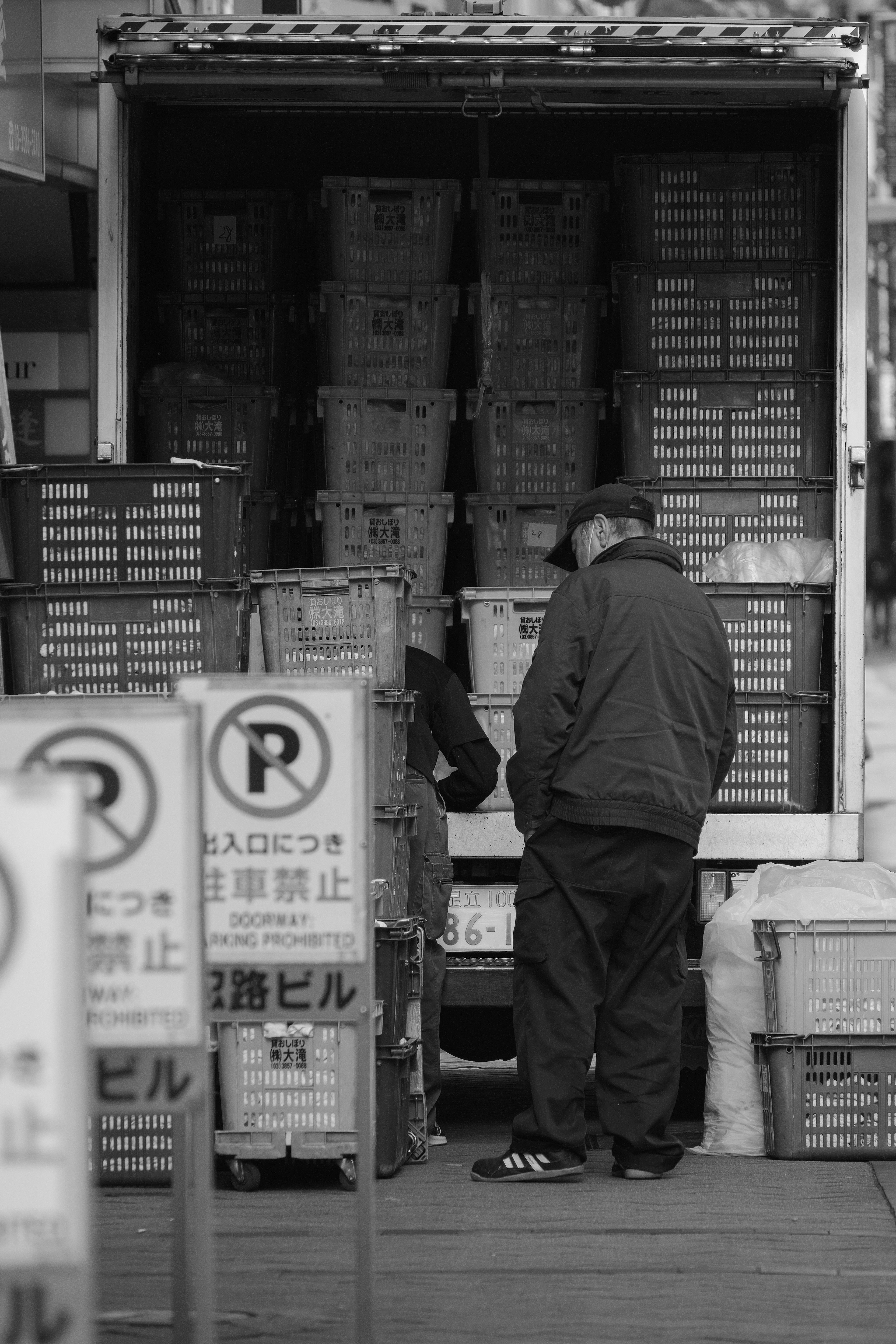 黒と白のトーンで、荷台の中に詰まった箱を見つめる男性の姿