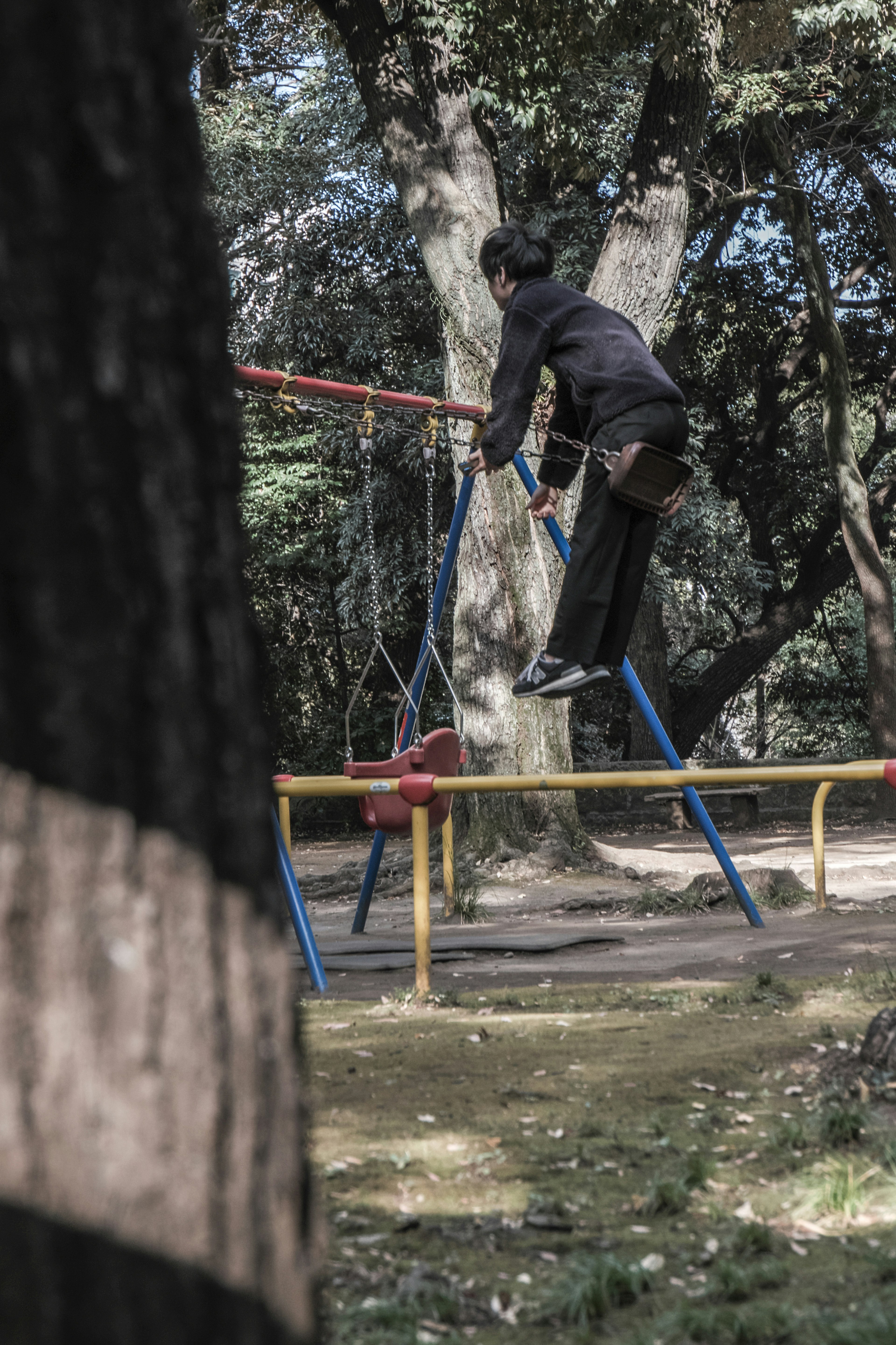 Un garçon se balançant sur une balançoire de parc entouré d'arbres verts