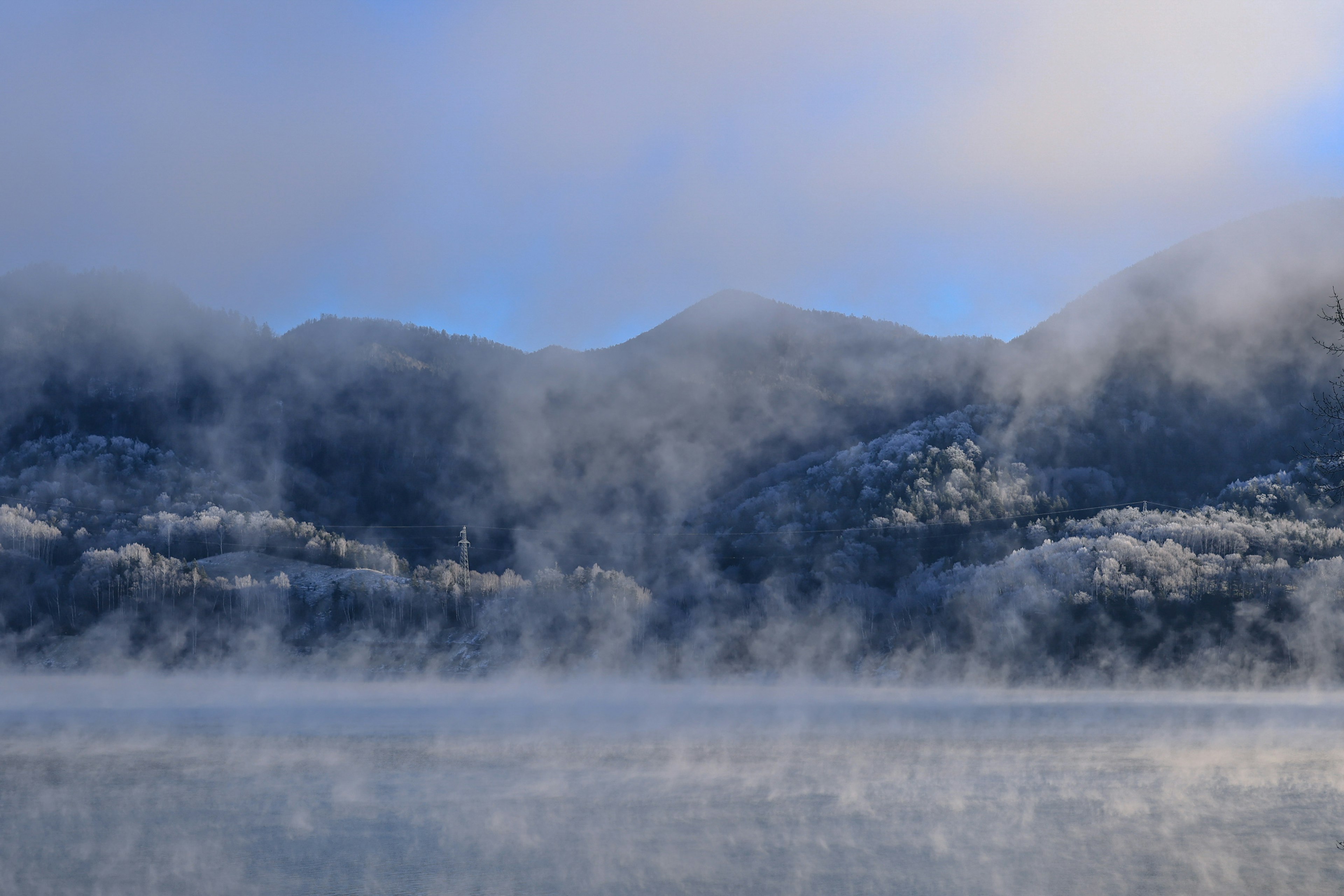 霧の中に浮かぶ雪に覆われた山々と冷たい湖面