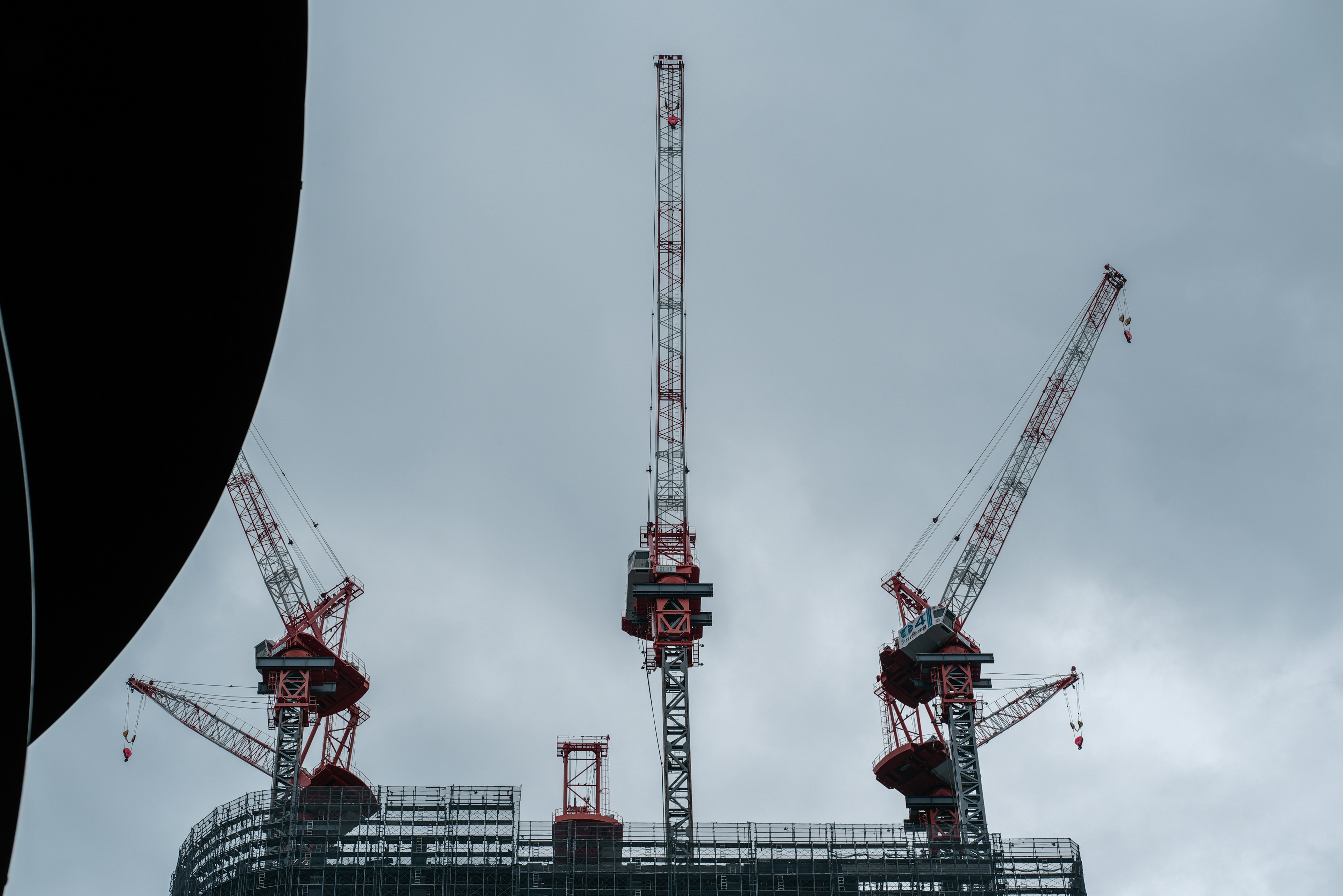 Red cranes towering over a construction site under a gray sky