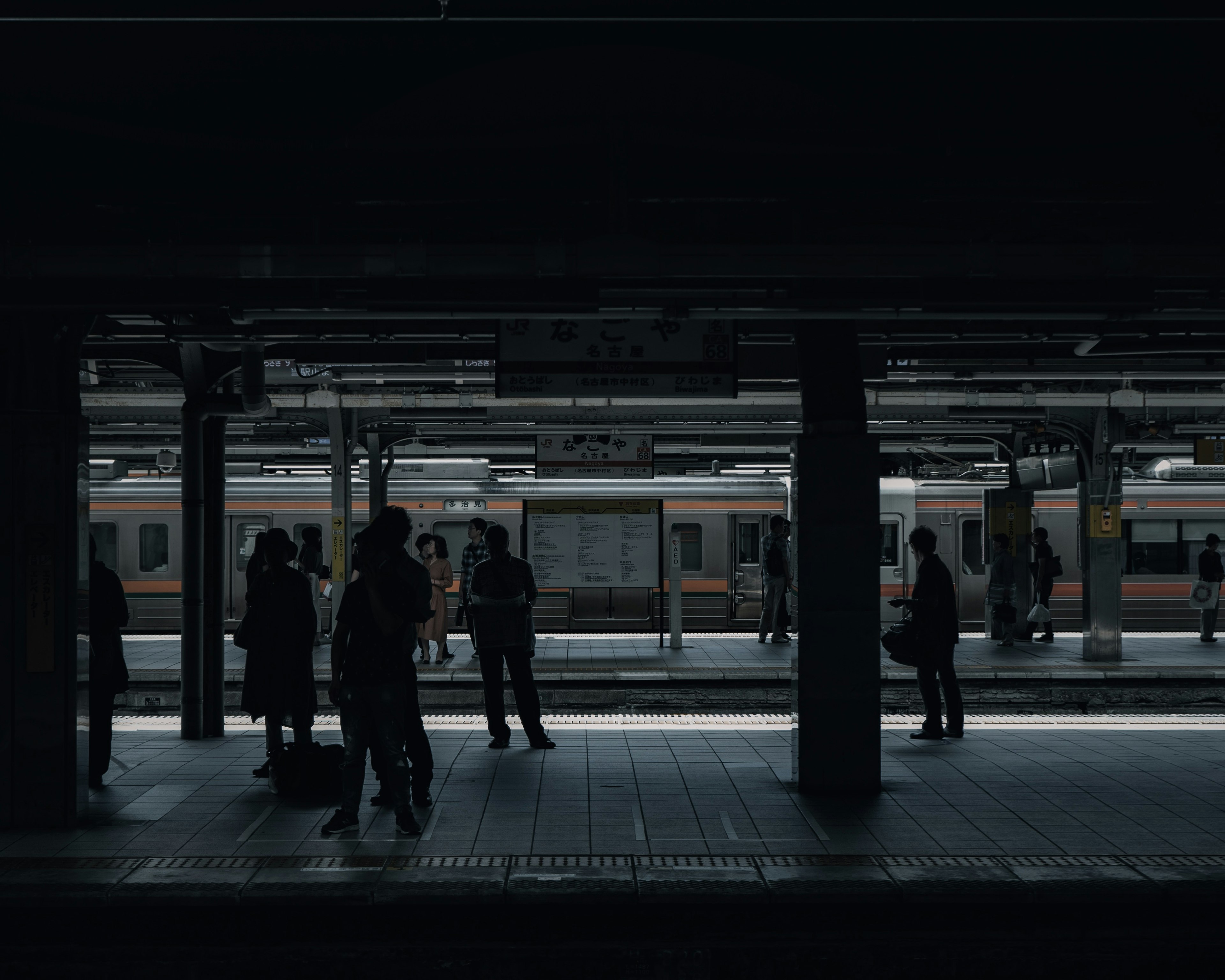 Silhouettes de personnes sur une plateforme de train sombre avec un train en arrière-plan