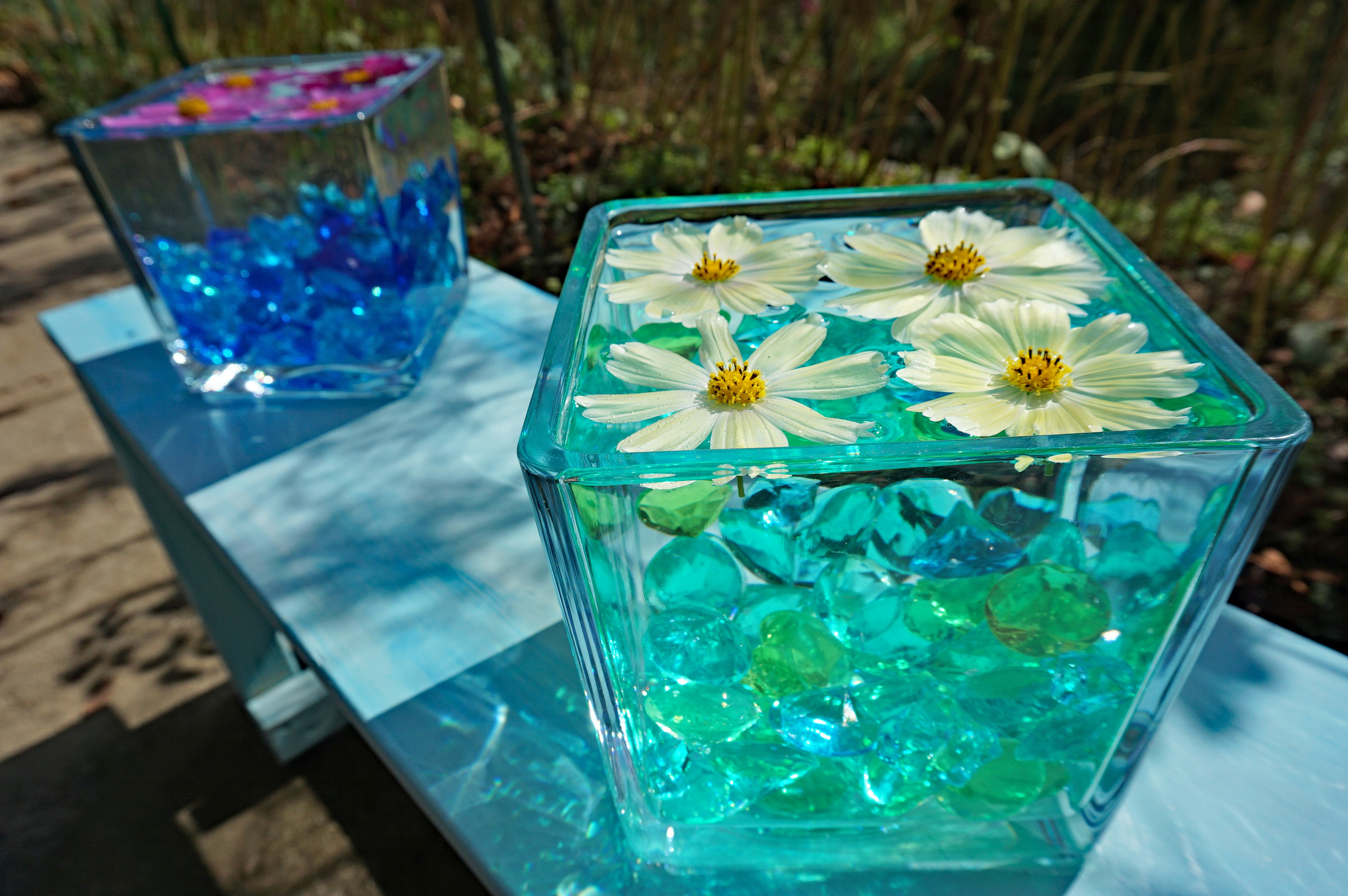 Transparente Behälter mit Blumen und bunten Edelsteinen in blauem Wasser