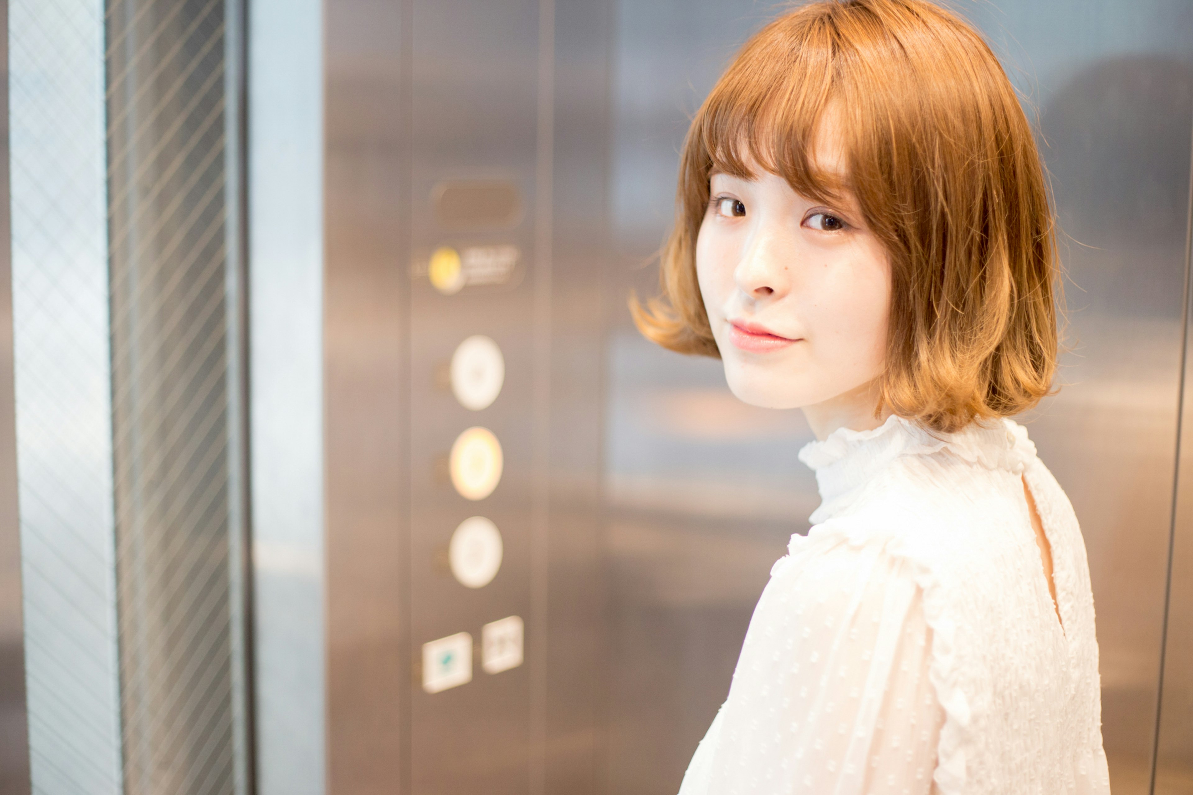 Portrait of a woman turning in an elevator featuring bright hair and a white outfit