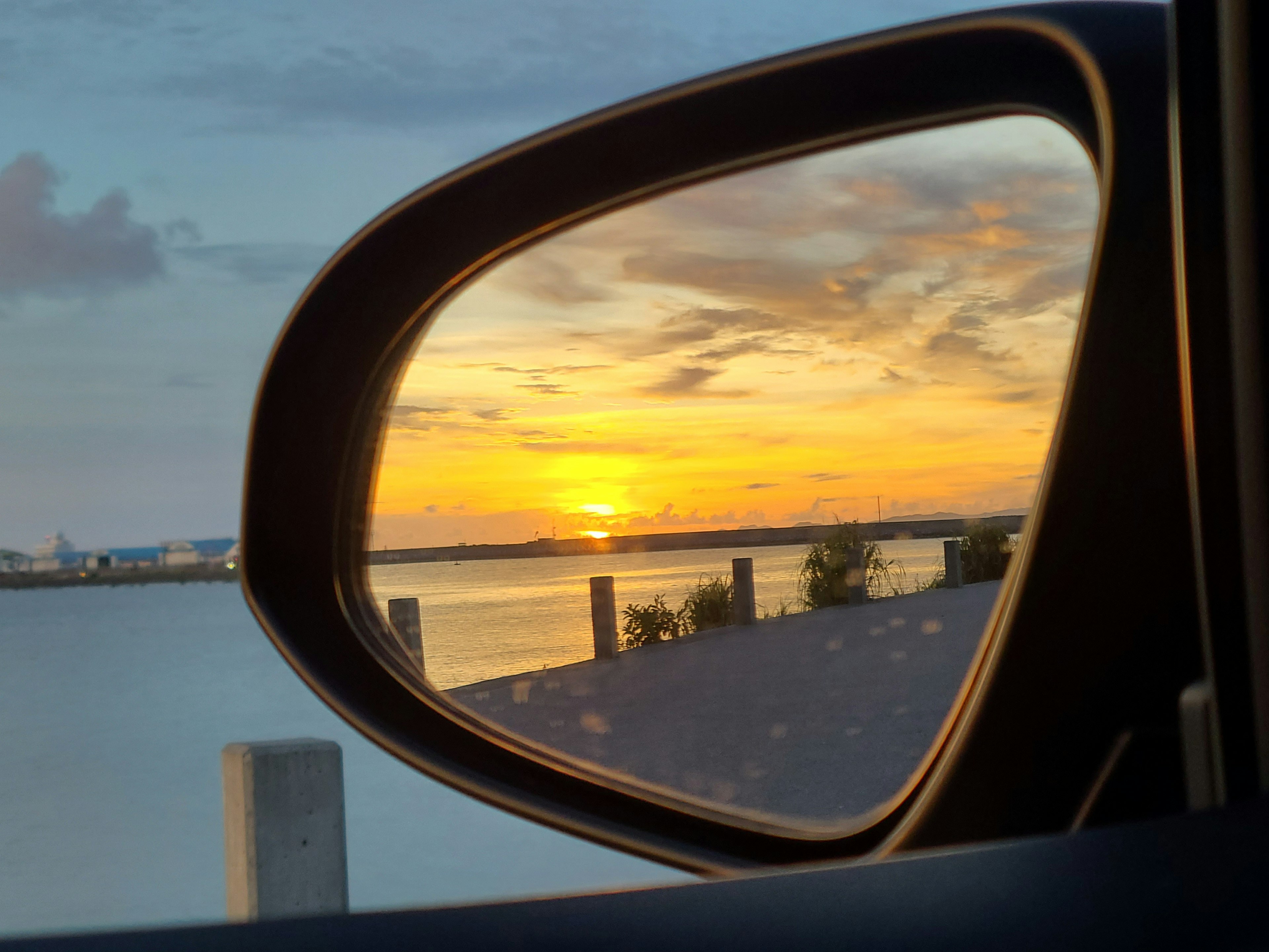 Sunset reflected in a car side mirror over a calm water surface