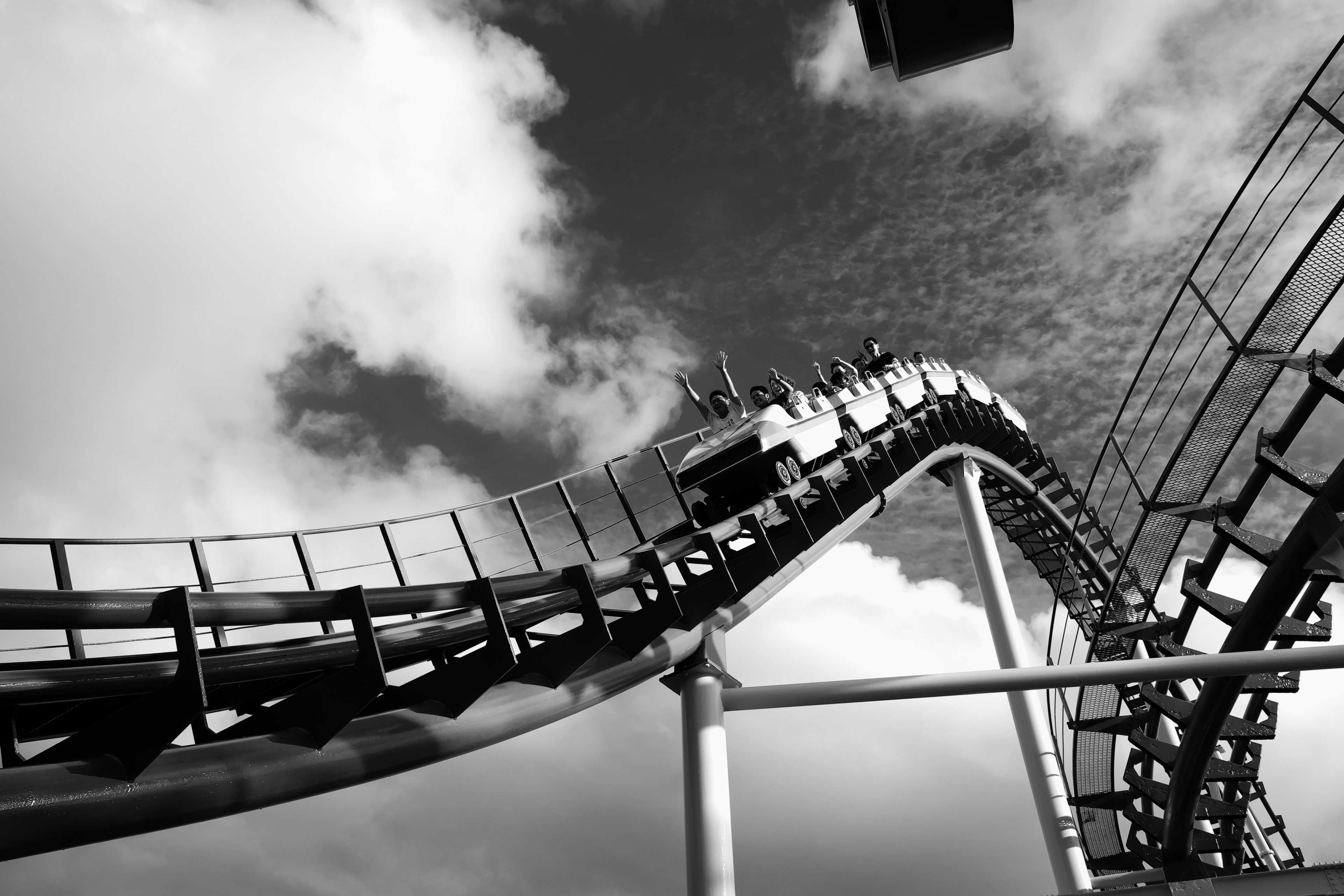 Montaña rusa en blanco y negro ascendiendo contra un cielo nublado