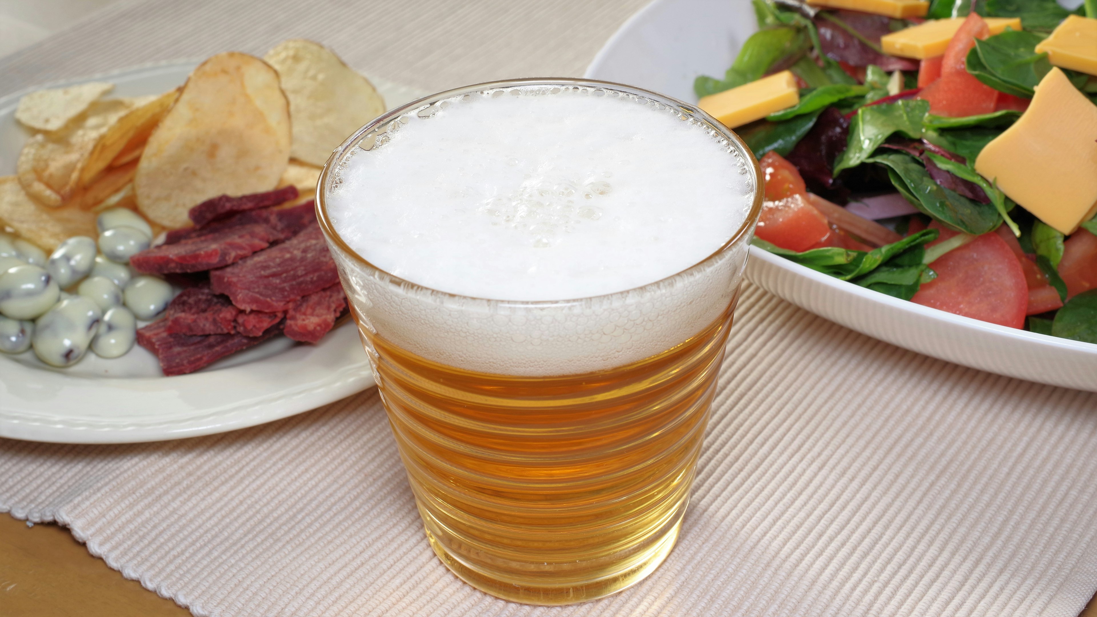 A glass of beer alongside a plate of snacks and a fresh salad