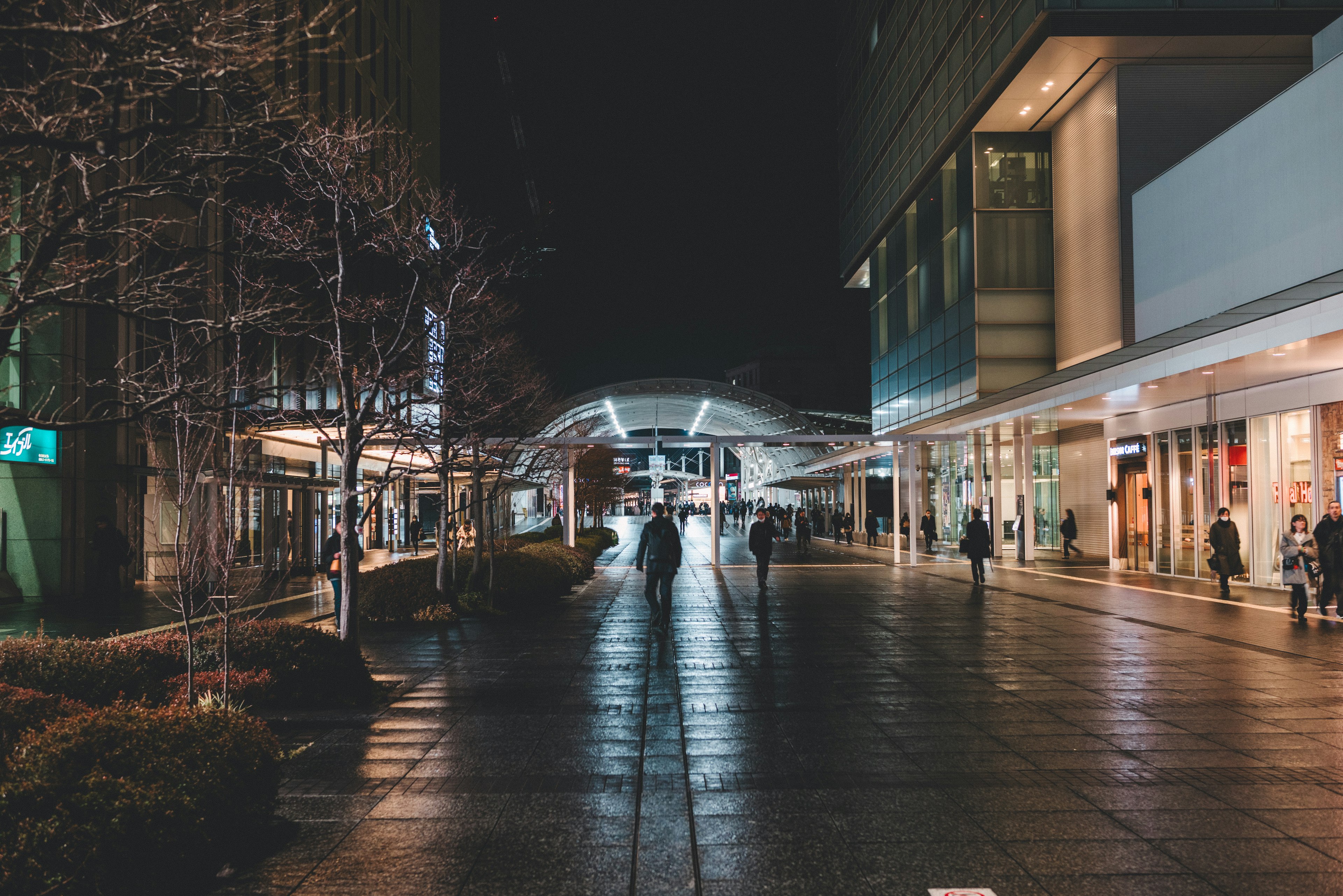 Des gens marchant dans une scène urbaine nocturne avec un sol réfléchissant et un éclairage lumineux