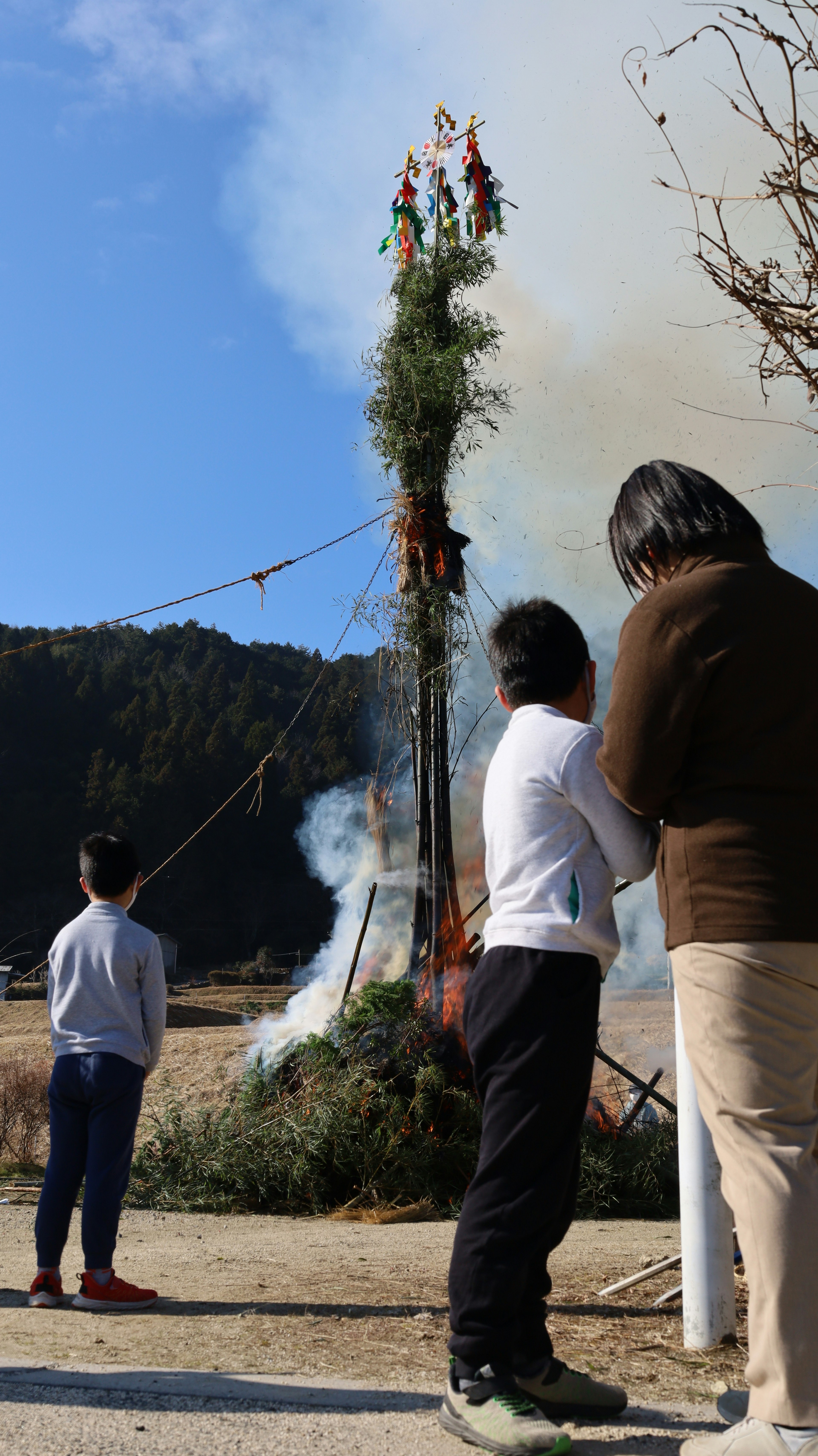 子供たちと大人が煙の中で火を見守る風景