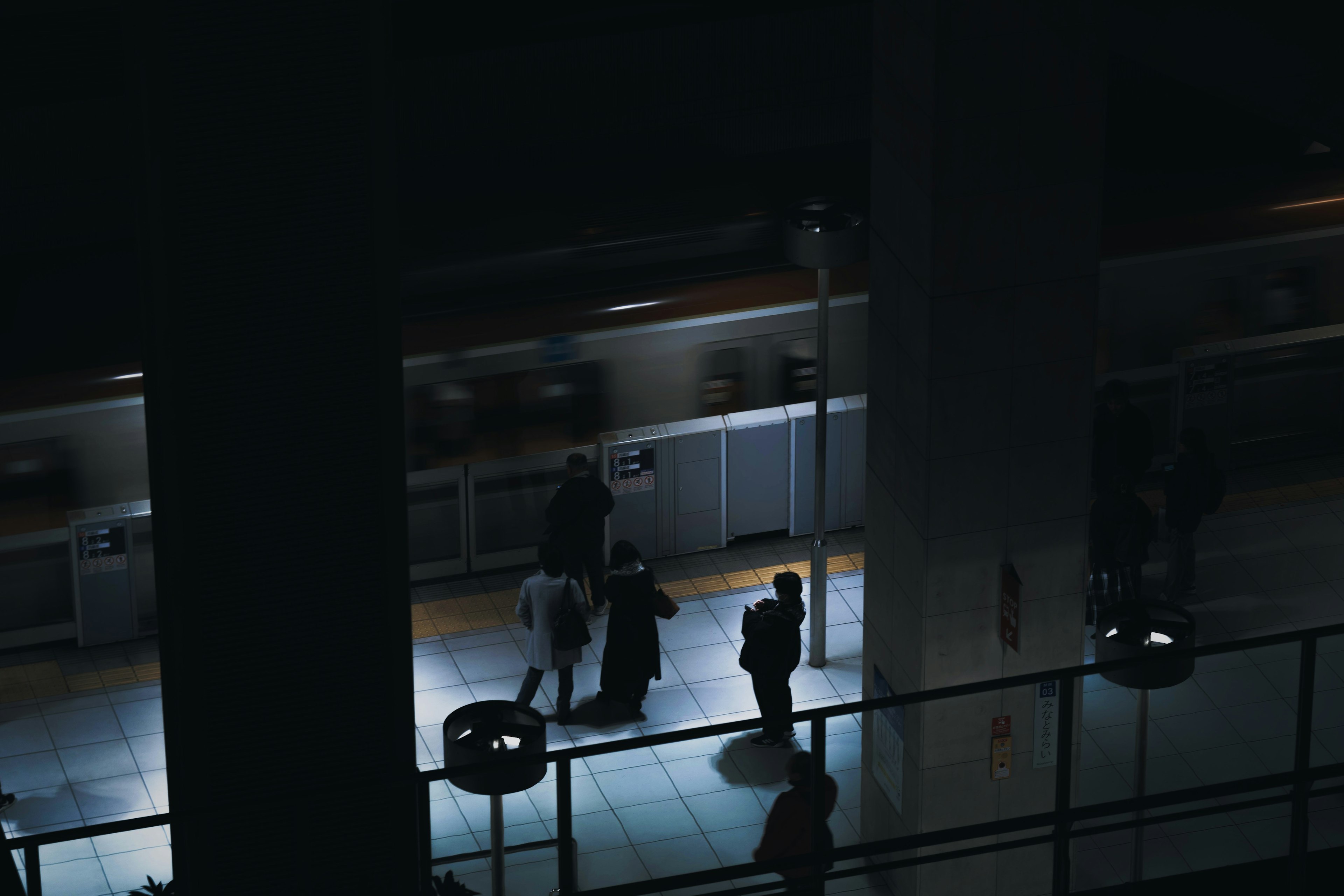 People walking in a dark train station platform with lighting