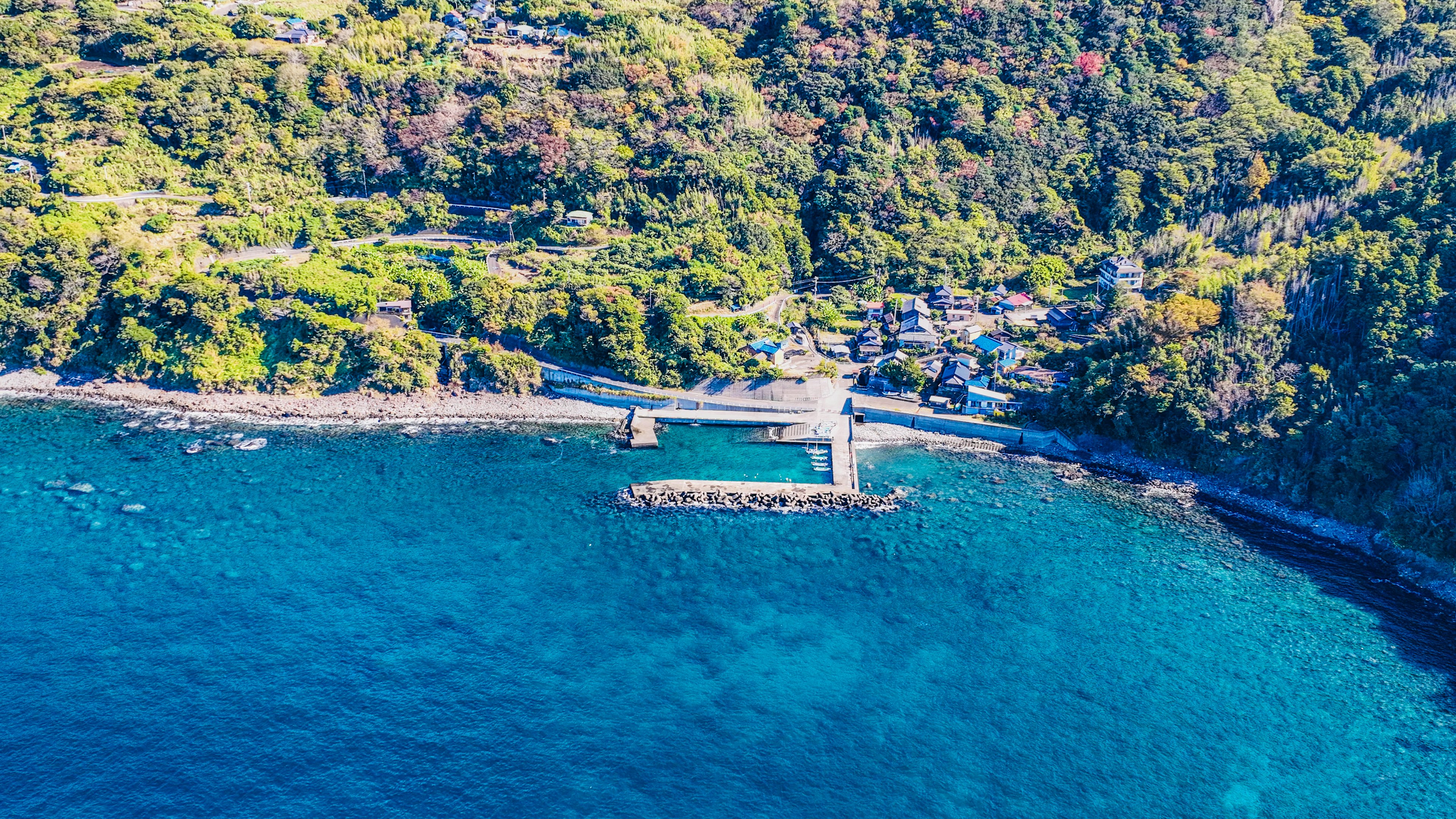 Aerial view of a small harbor surrounded by blue sea and green hills