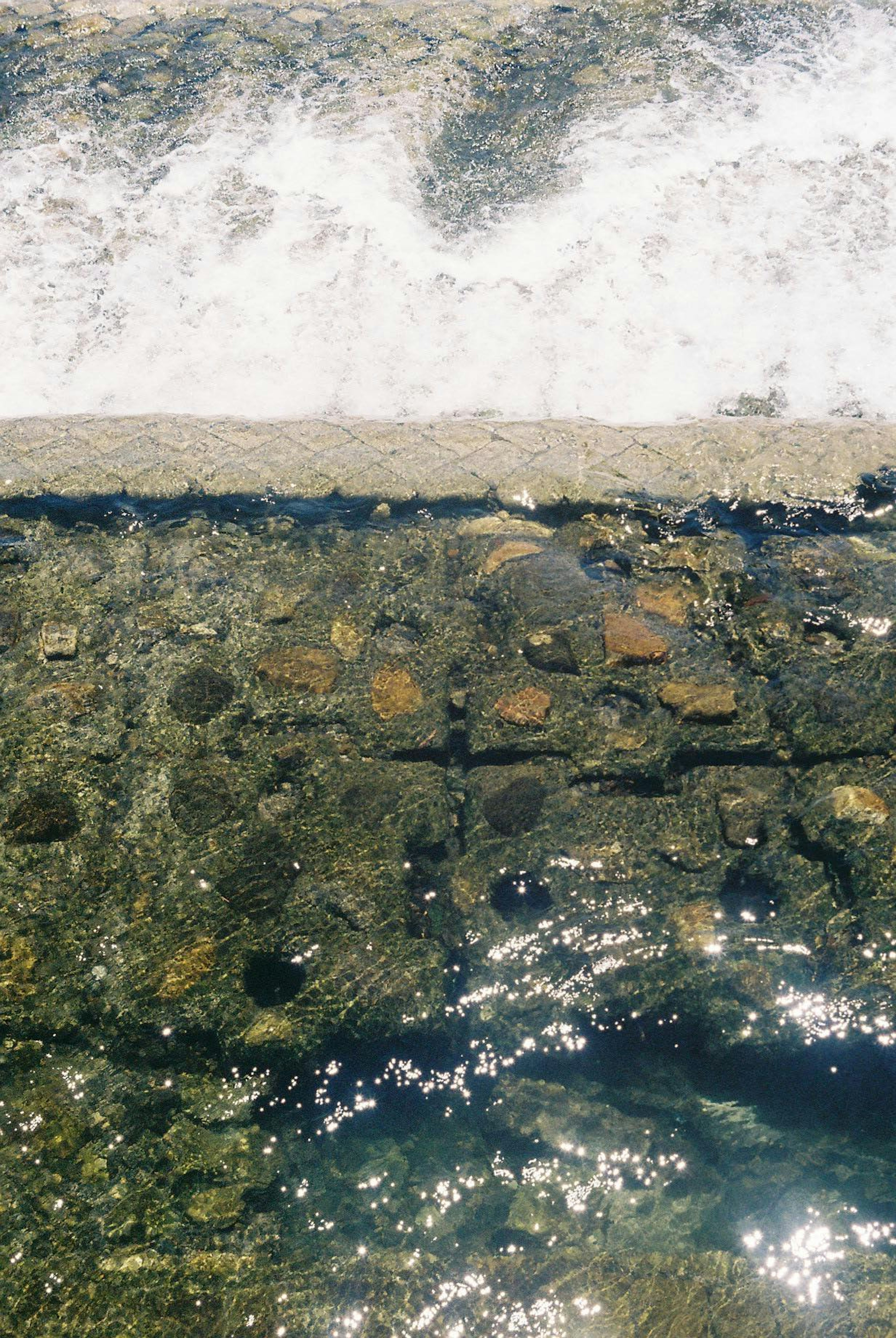 Wasseroberfläche, die Licht reflektiert, mit strukturierten Steinen in einer Flusslandschaft