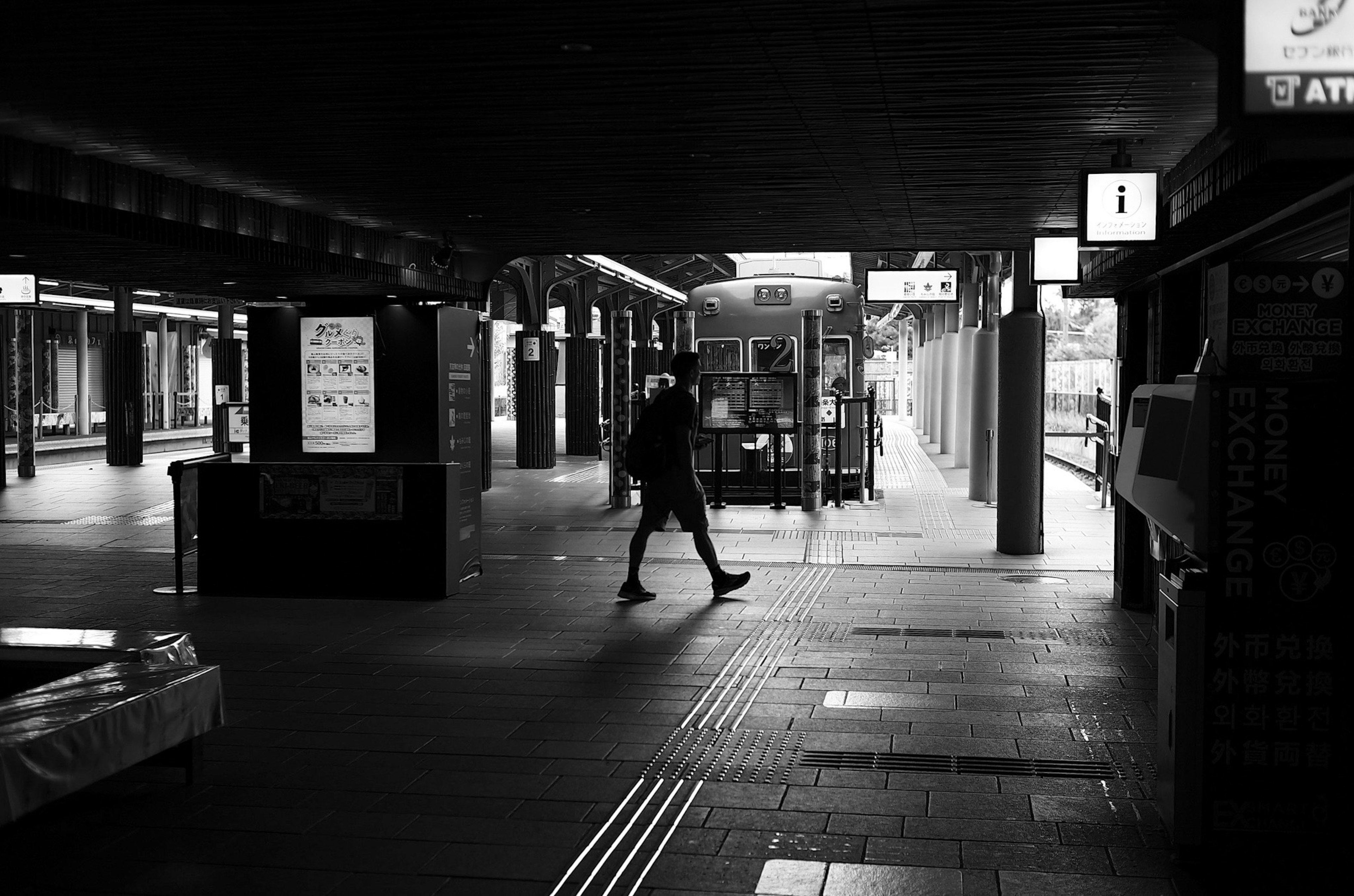 Seseorang berjalan di dalam stasiun hitam putih