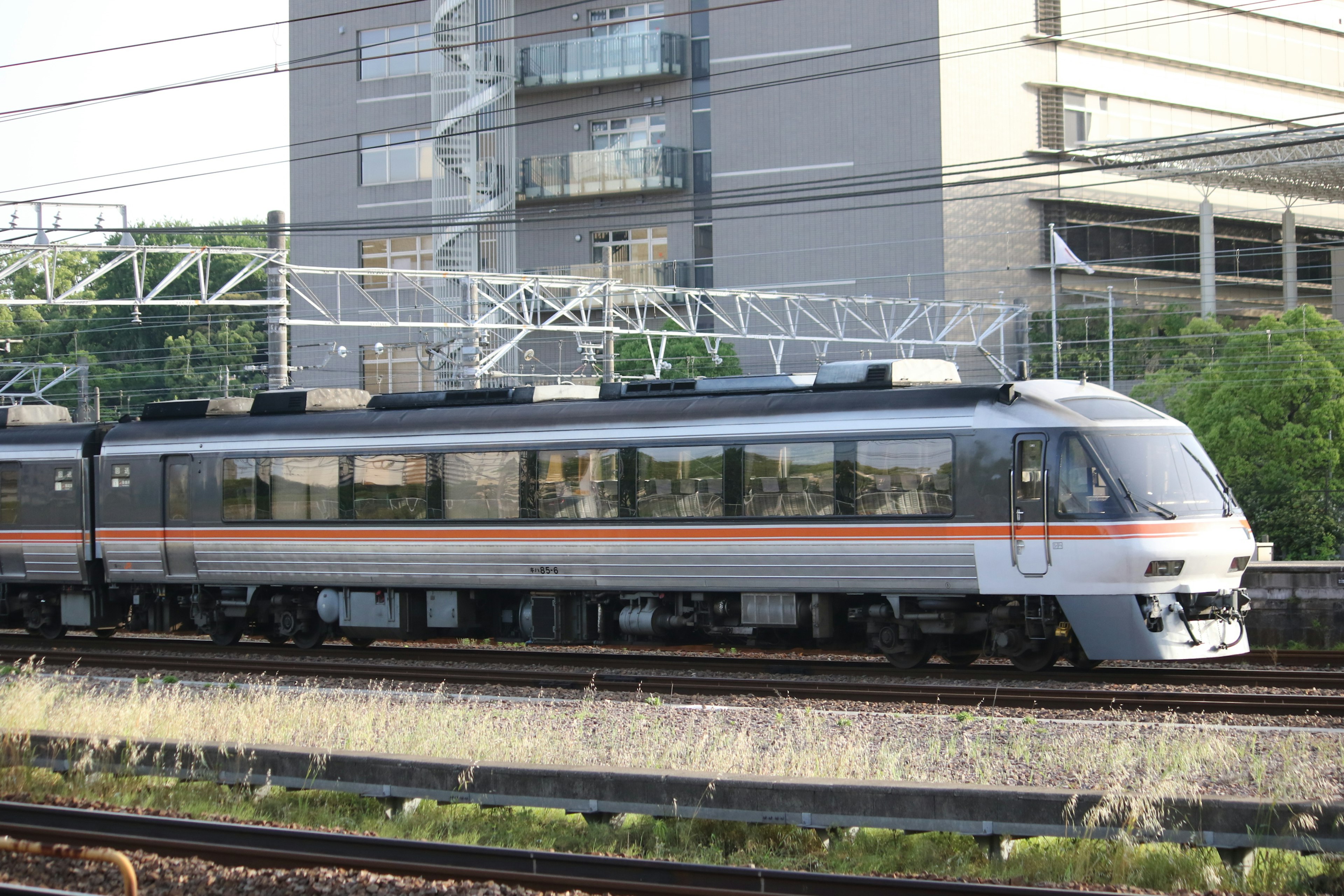 Treno espresso argento sui binari con un edificio moderno sullo sfondo