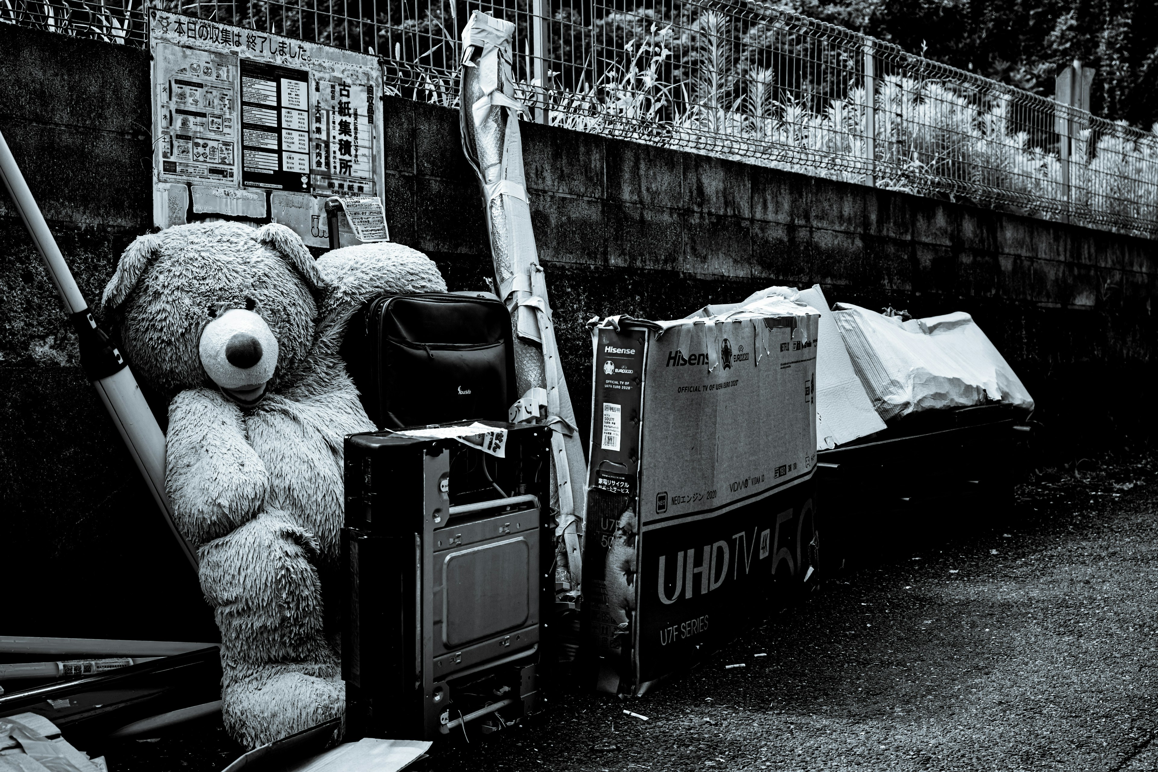 A large teddy bear sitting among discarded items and trash