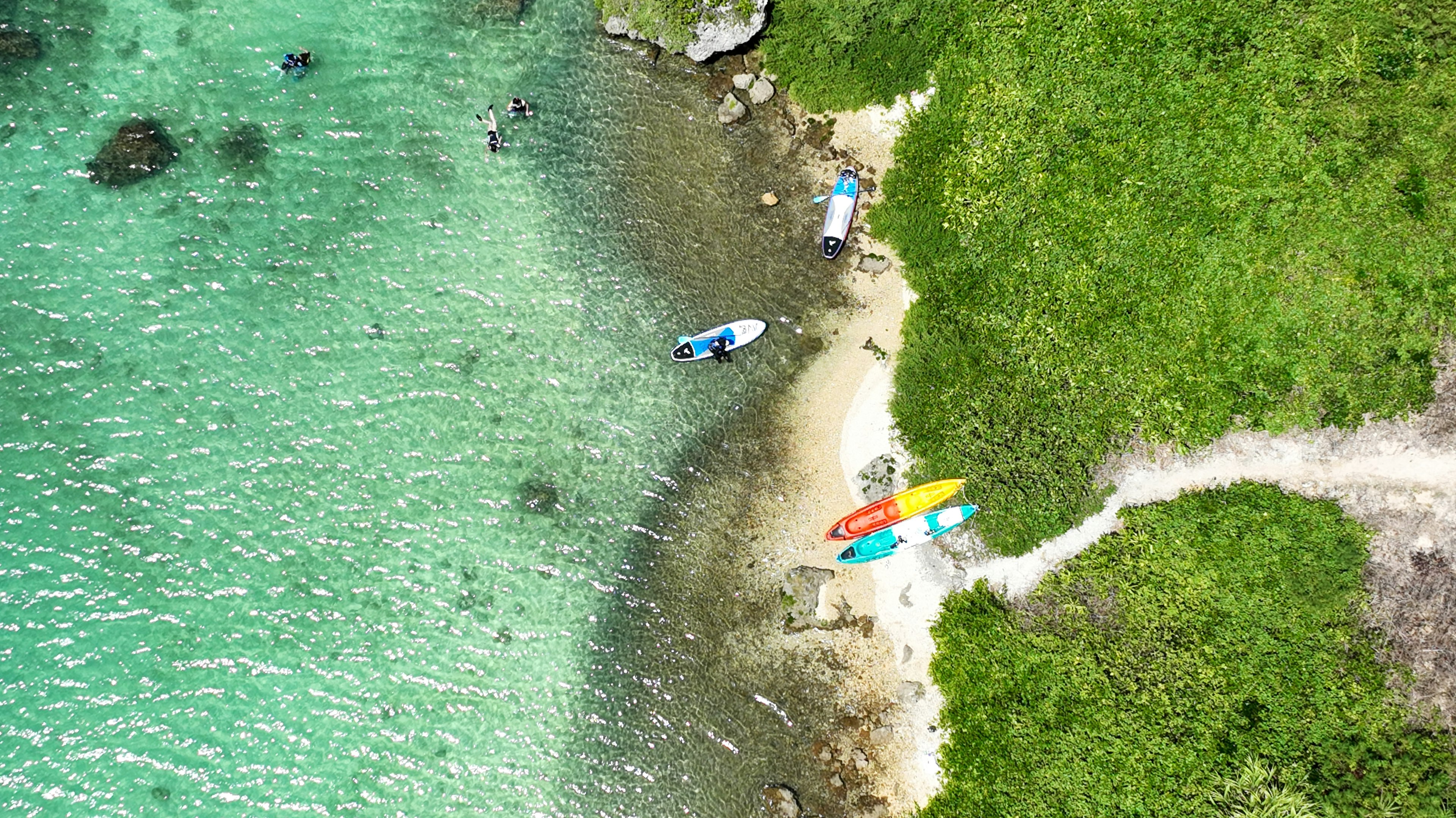 Aerial view of a beach with turquoise water and green grass several kayaks are docked on the shore