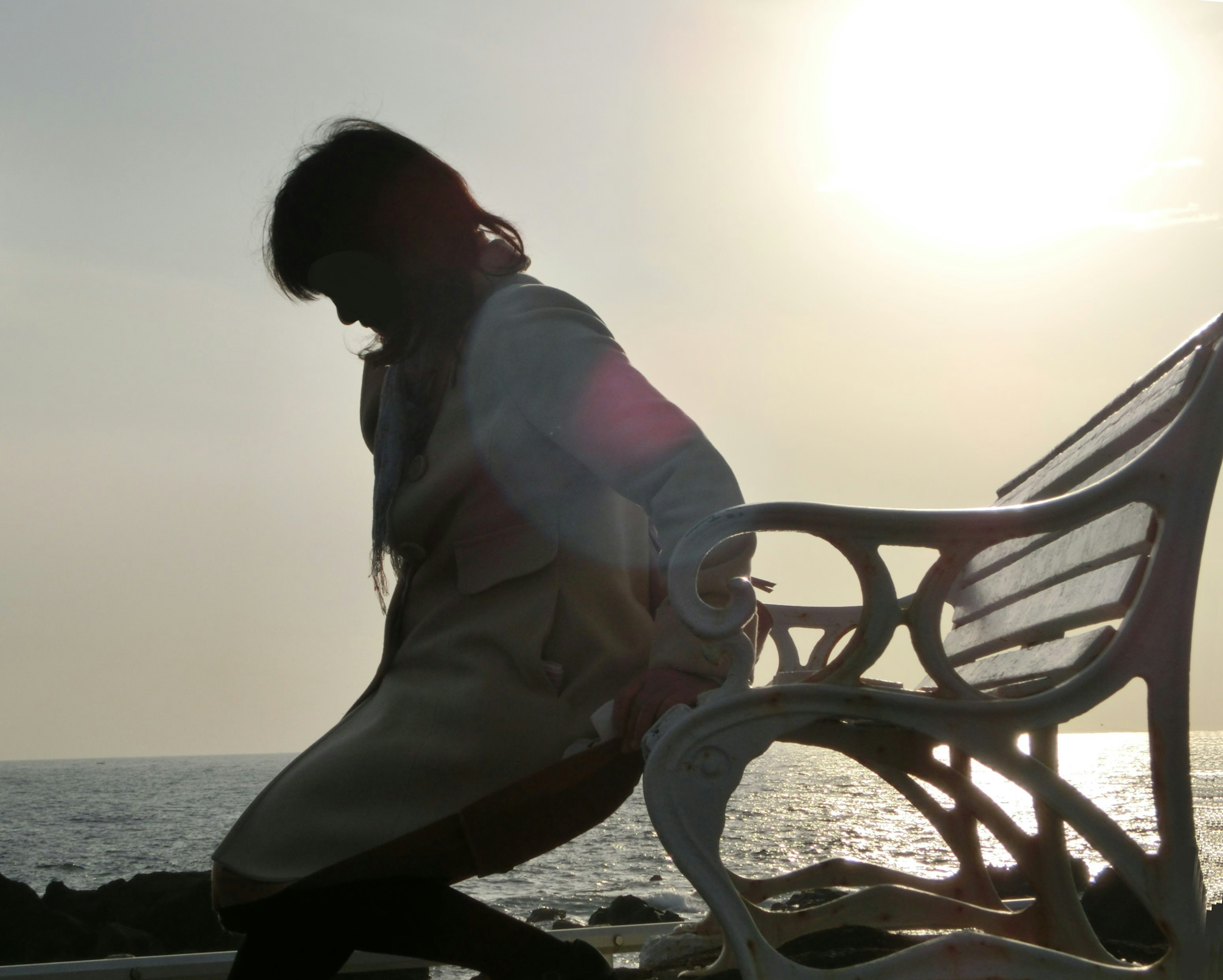 Silhouette einer Frau, die auf einem Stuhl am Meer sitzt, mit einem leuchtenden Sonnenuntergang im Hintergrund