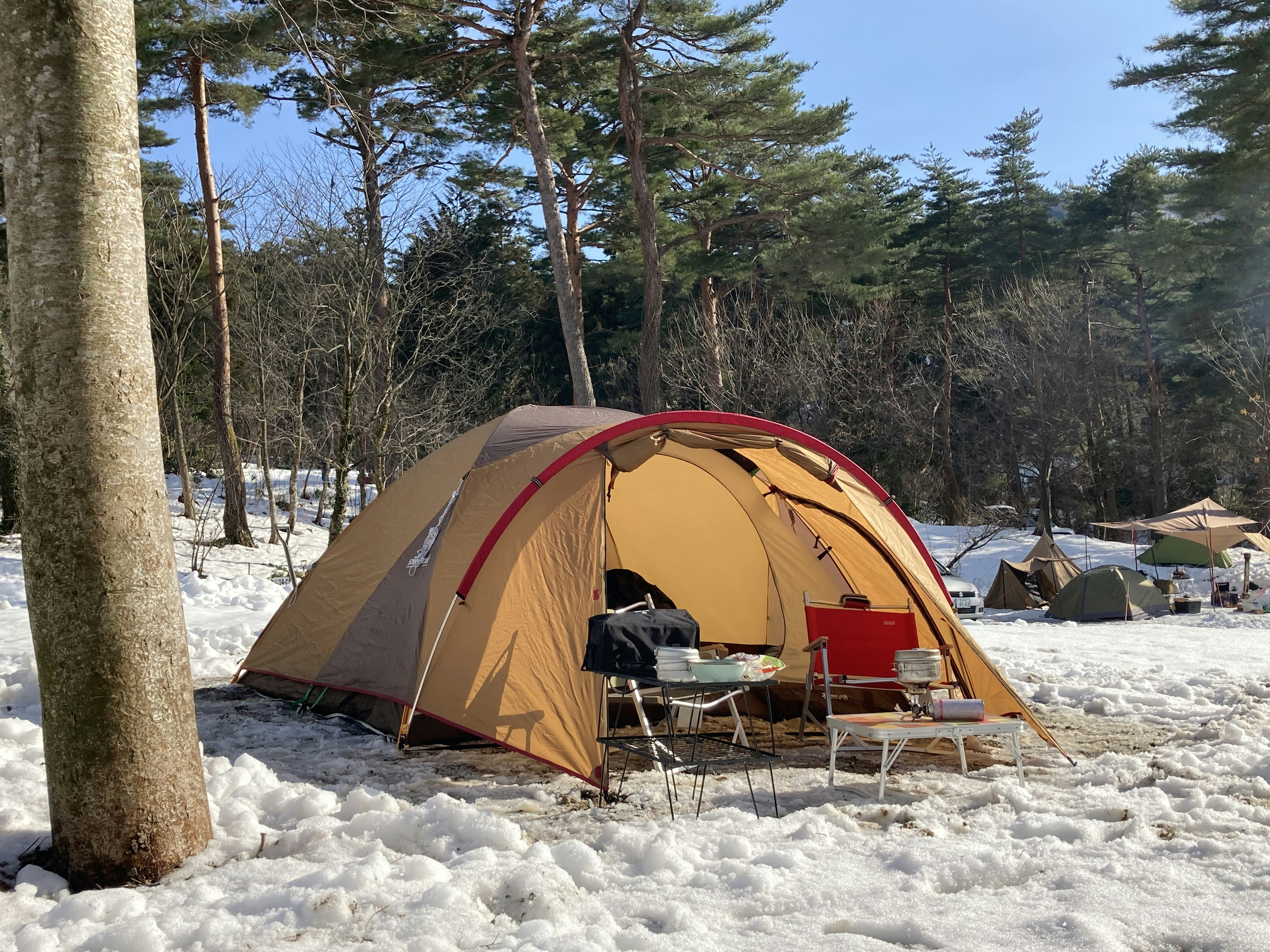 Brown tent set up in a snowy campsite with red chairs