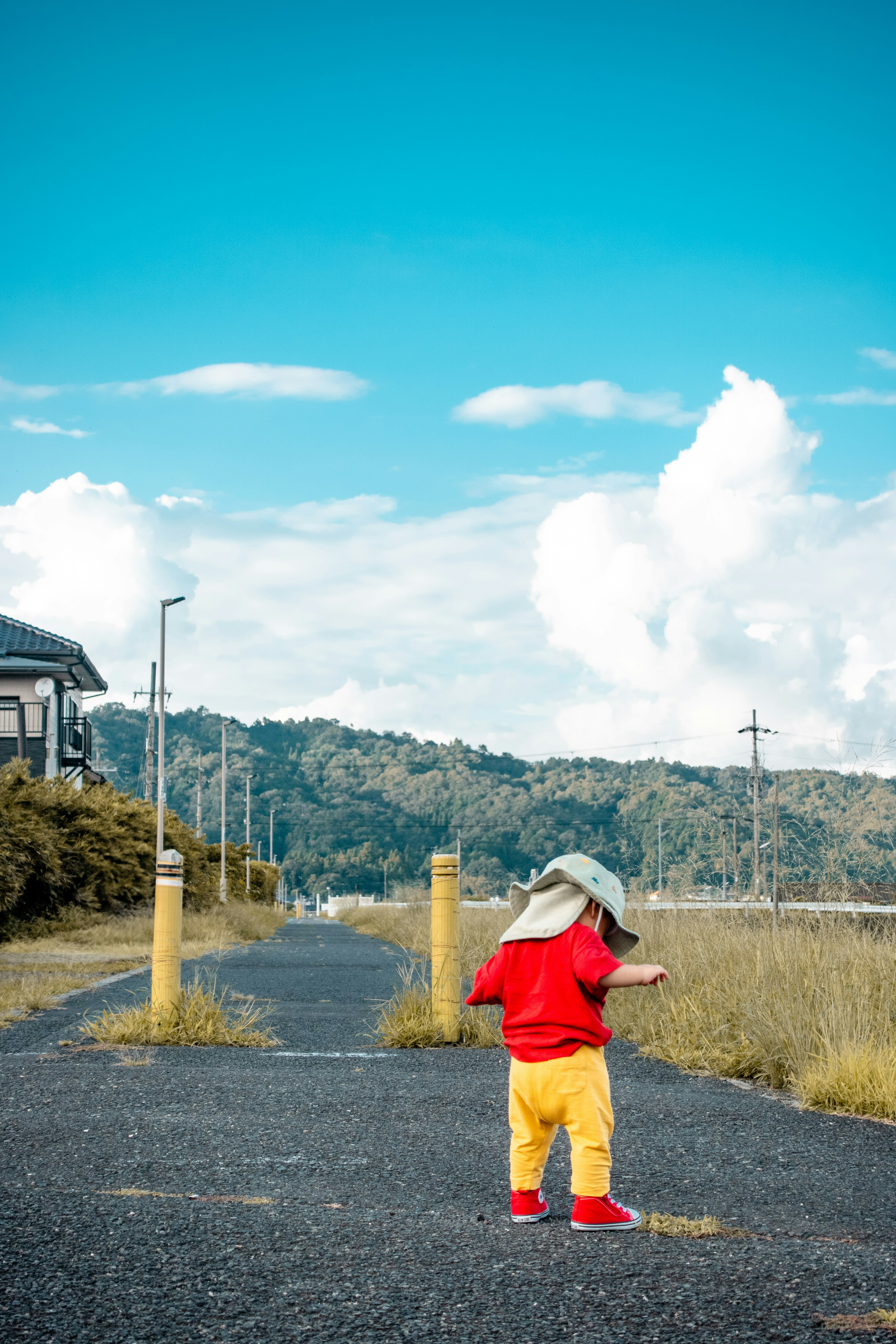 赤い服と黄色いズボンを着た子供が道を歩いている風景