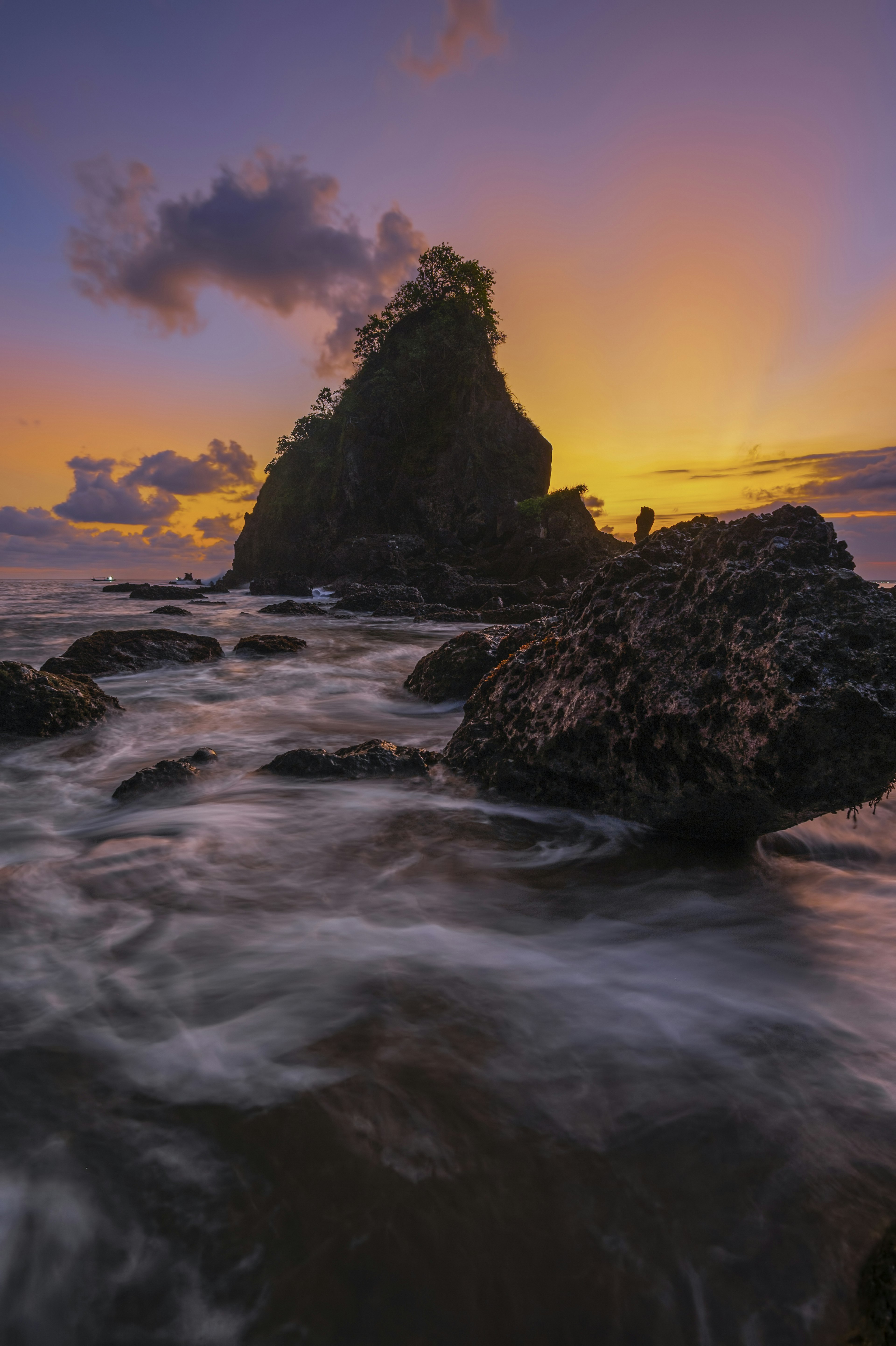 Formasi batu pantai dengan ombak saat matahari terbenam