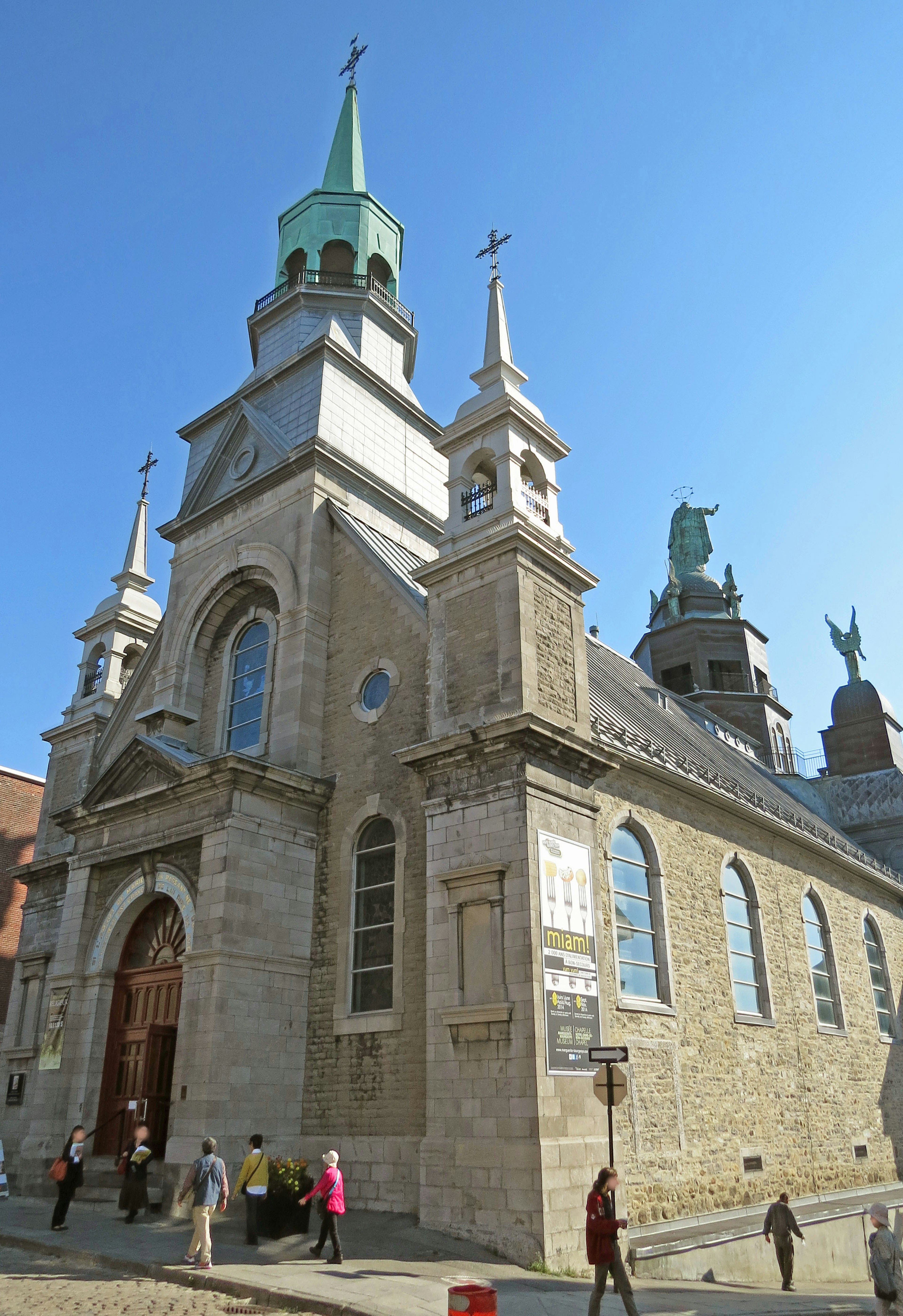 Extérieur d'une église historique avec des flèches vertes et de nombreuses personnes marchant autour