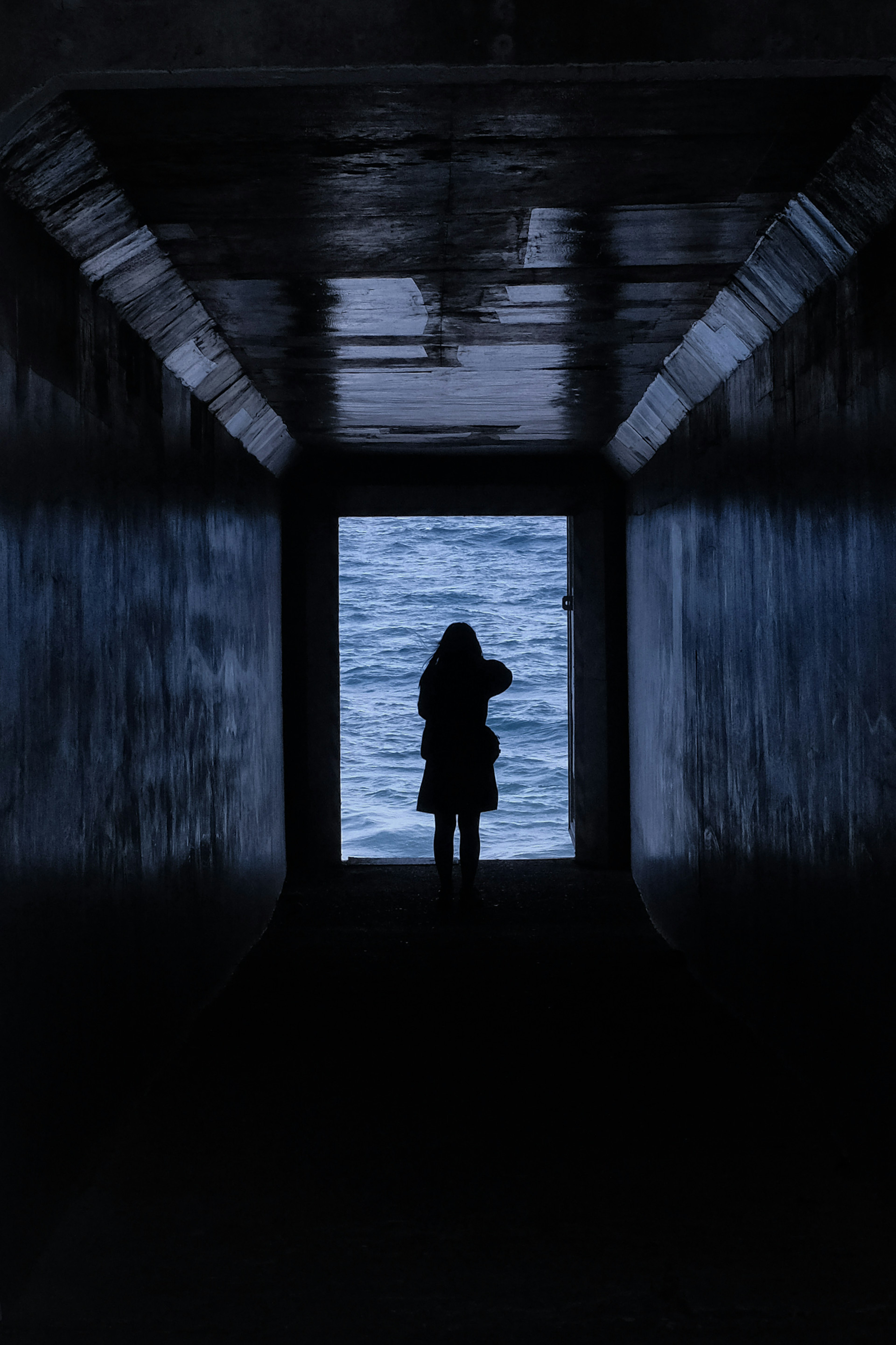 Silhouette of a person standing in a dark tunnel with a view of the blue sea