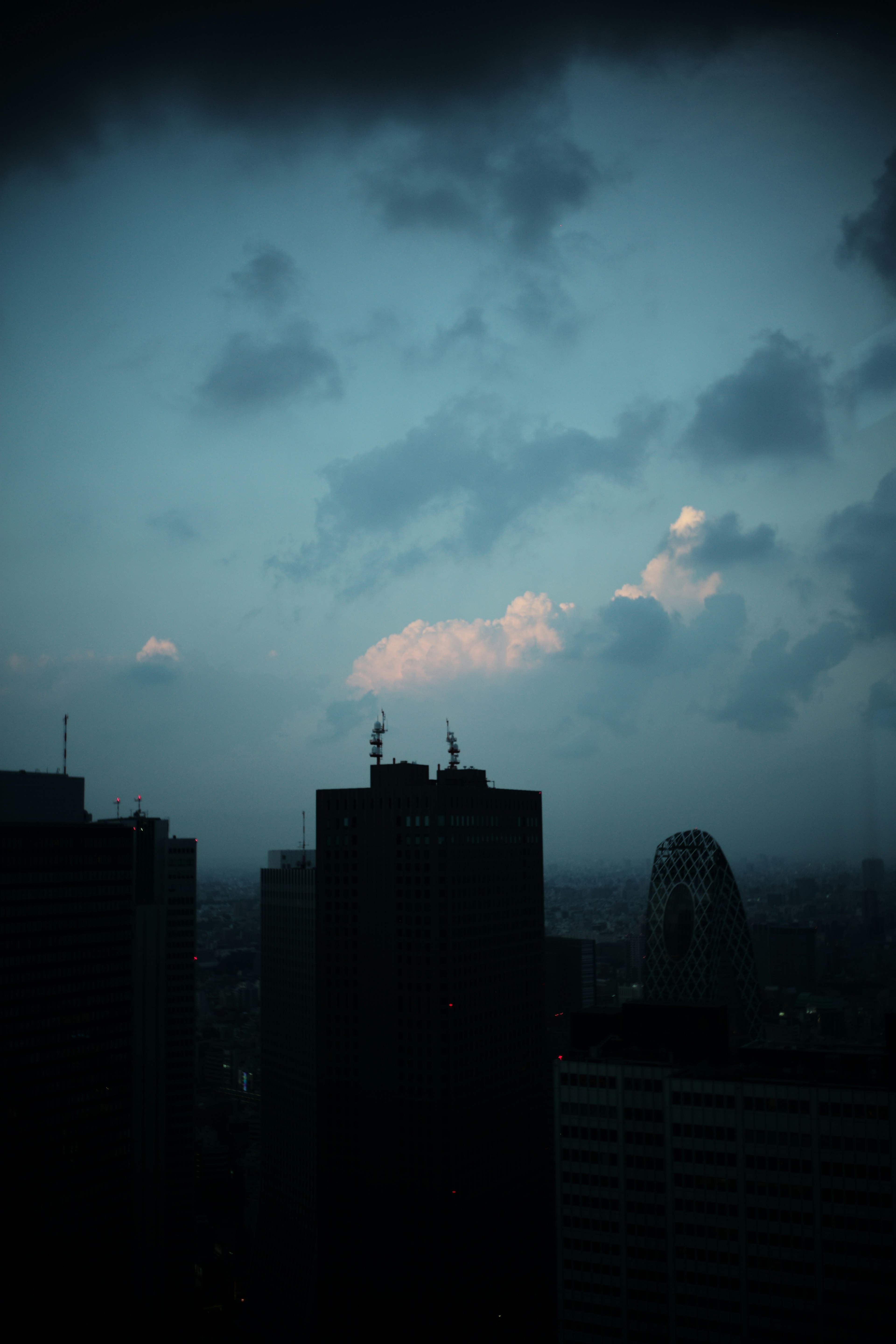 薄暗い空の下にそびえる高層ビル群と雲