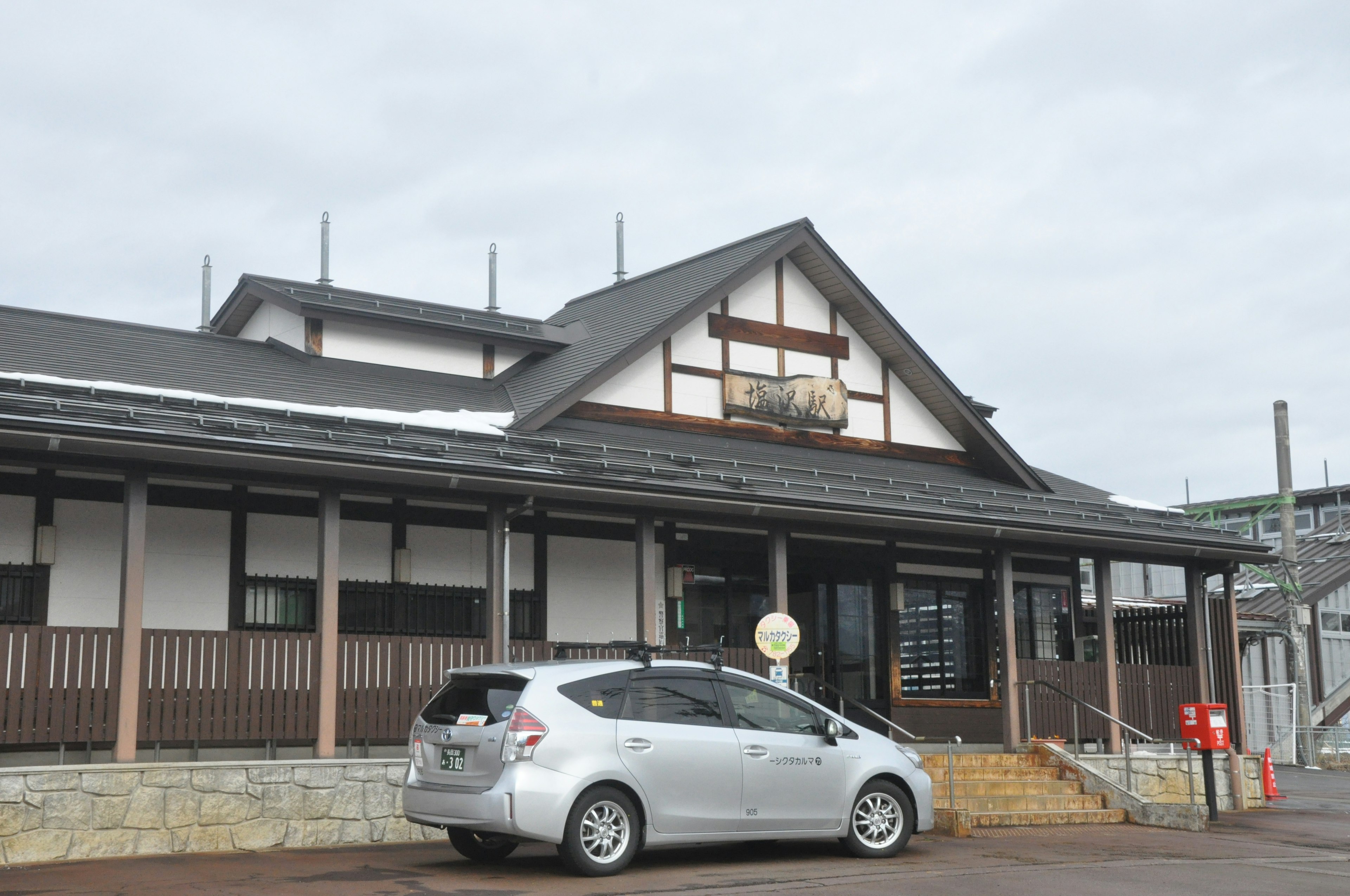 伝統的な日本の建築様式を持つ駅舎とその前に停まる車