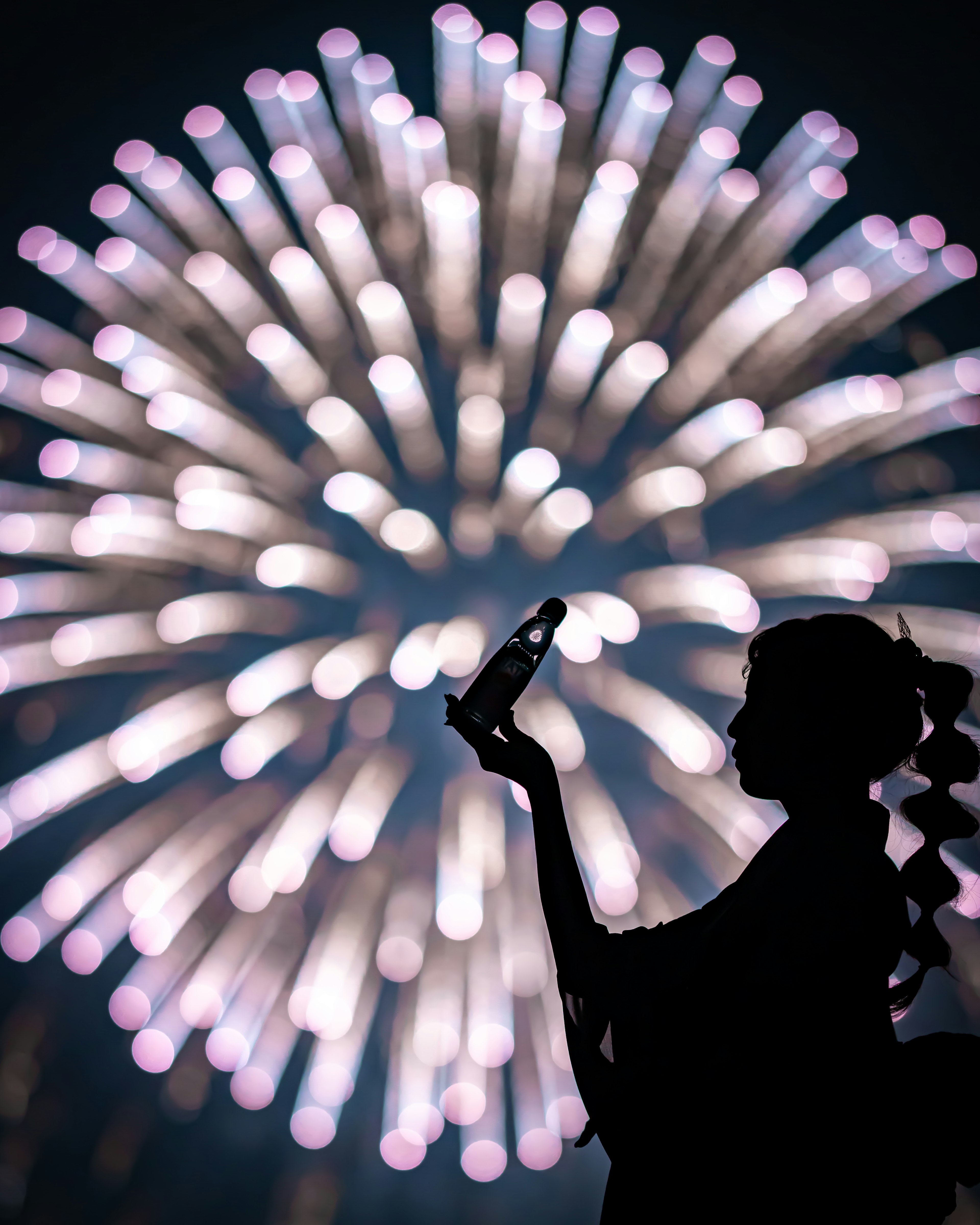 Silhouette einer Frau, die eine Coca-Cola-Flasche vor einem lebhaften Feuerwerk hält