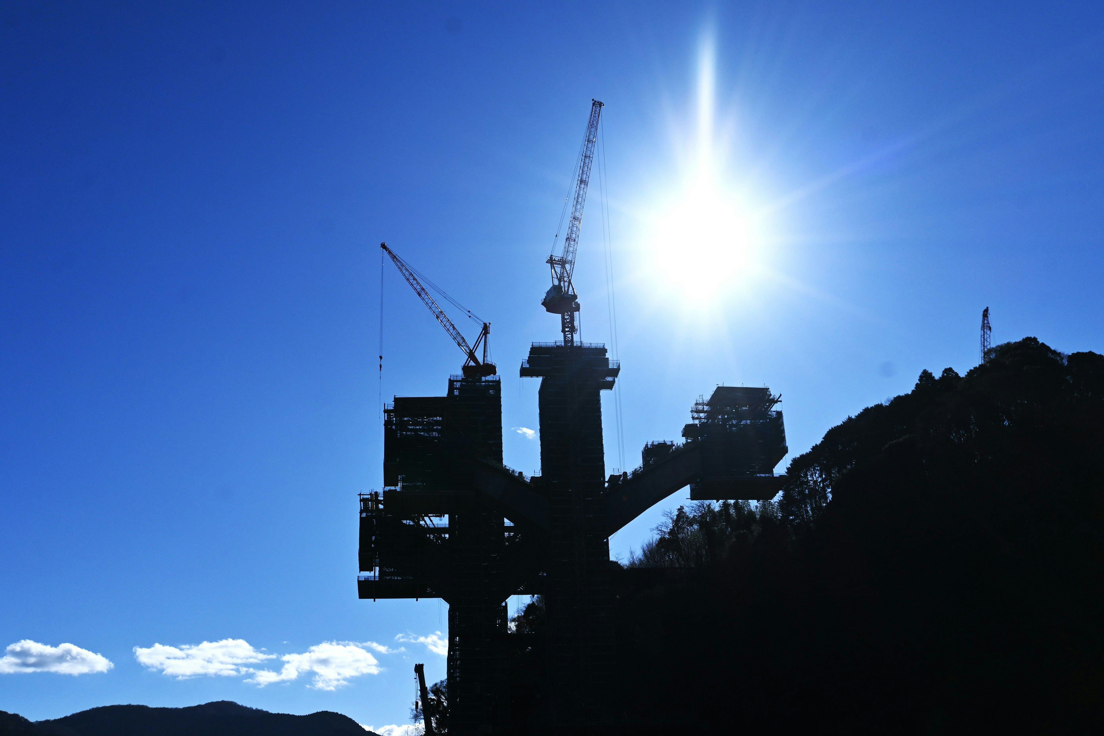 Silhouette of construction cranes and structures against a blue sky