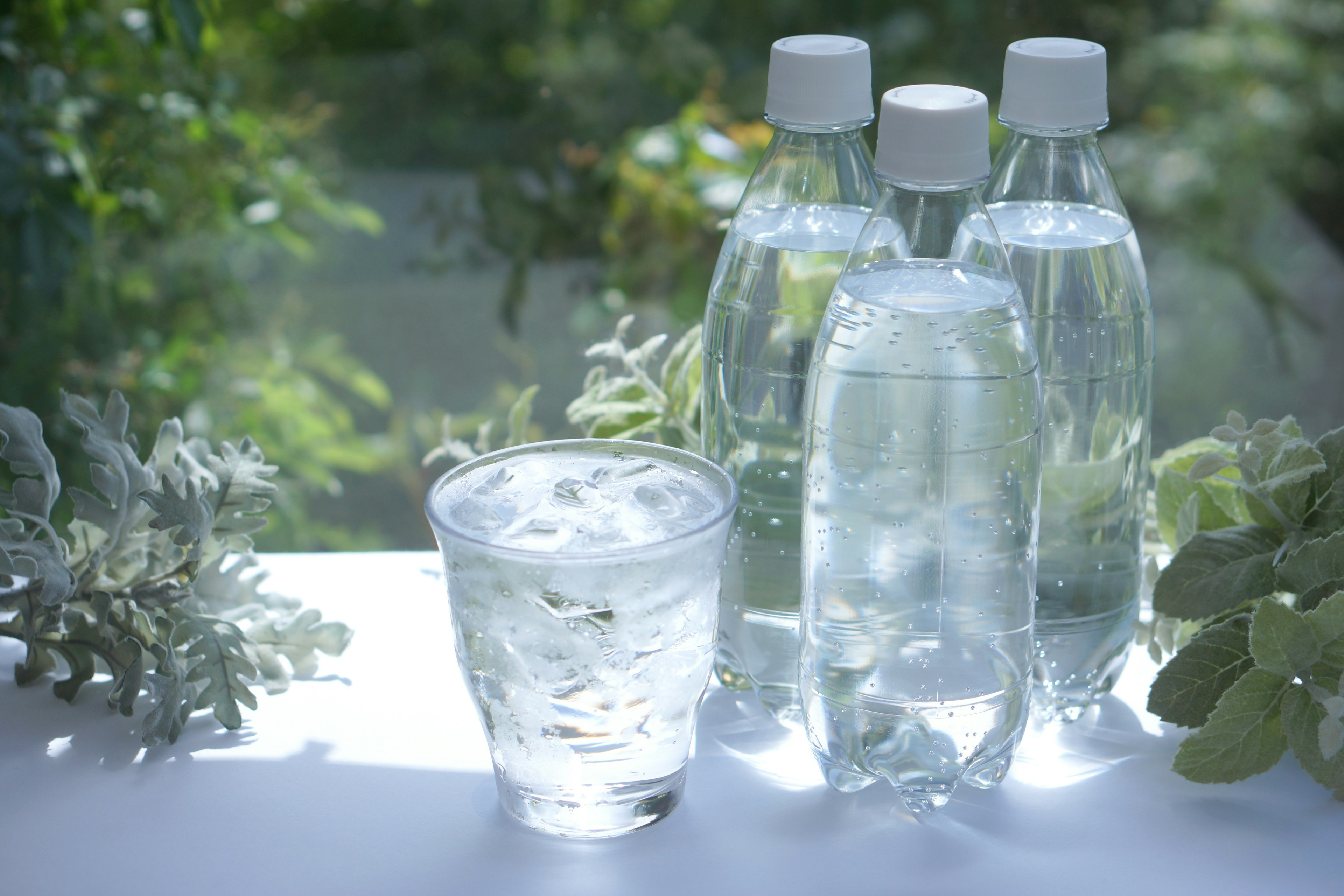 Imagen de un vaso de agua helada y varias botellas de agua con un fondo verde