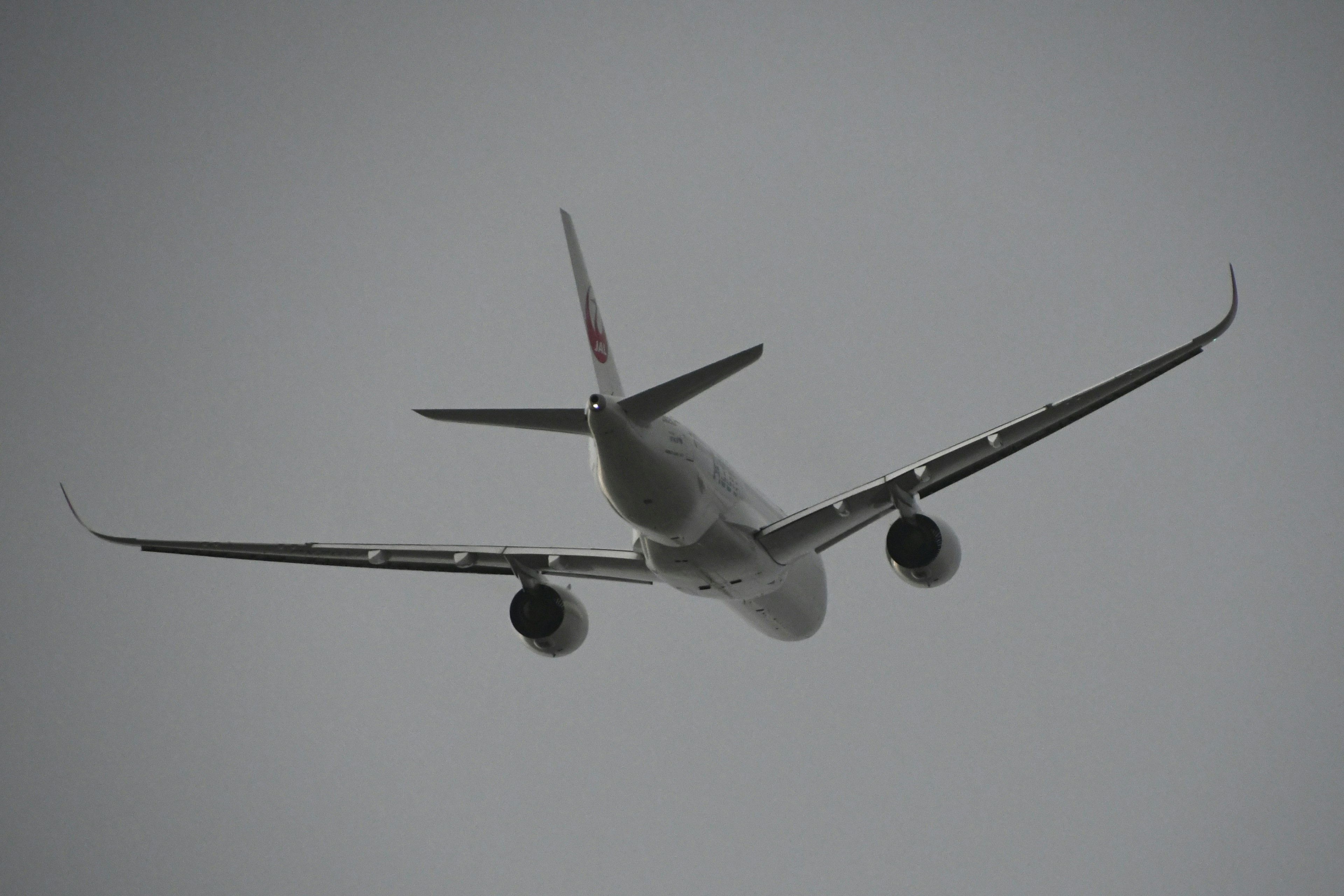 空を飛ぶ飛行機の後ろ姿 雲がかかった空を背景にしたシルエット