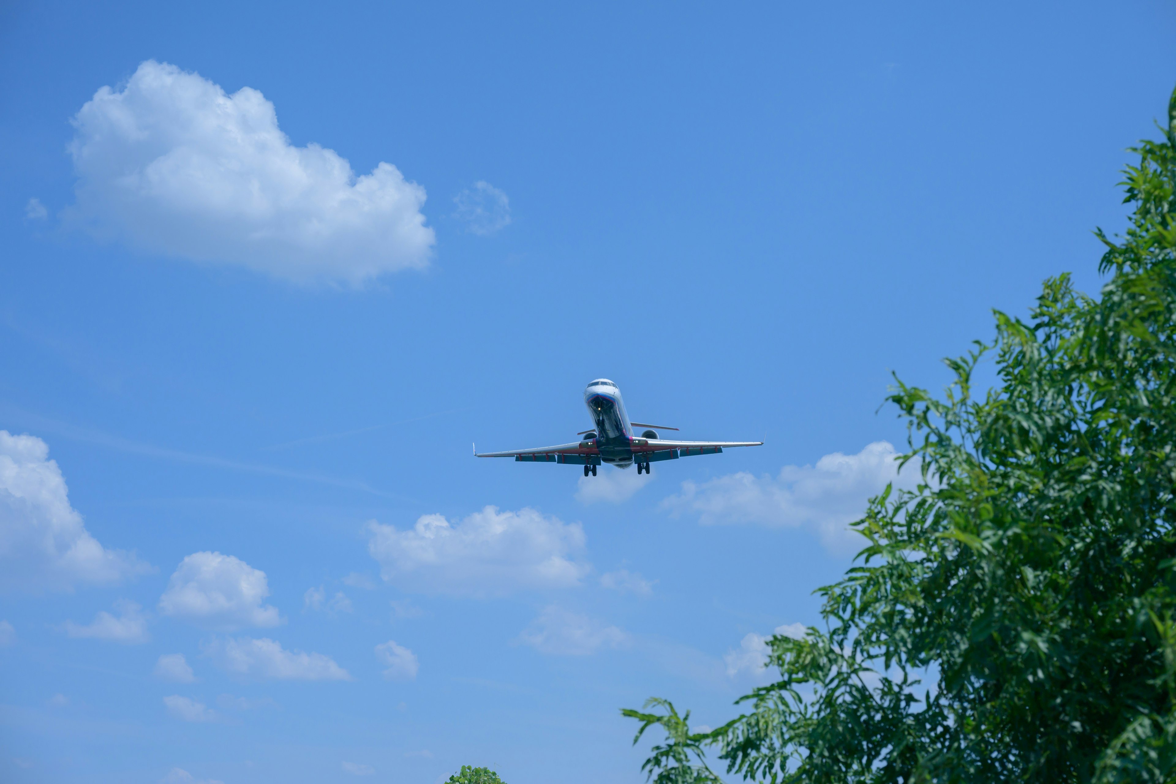 Un aereo che vola in un cielo blu con nuvole bianche e alberi verdi