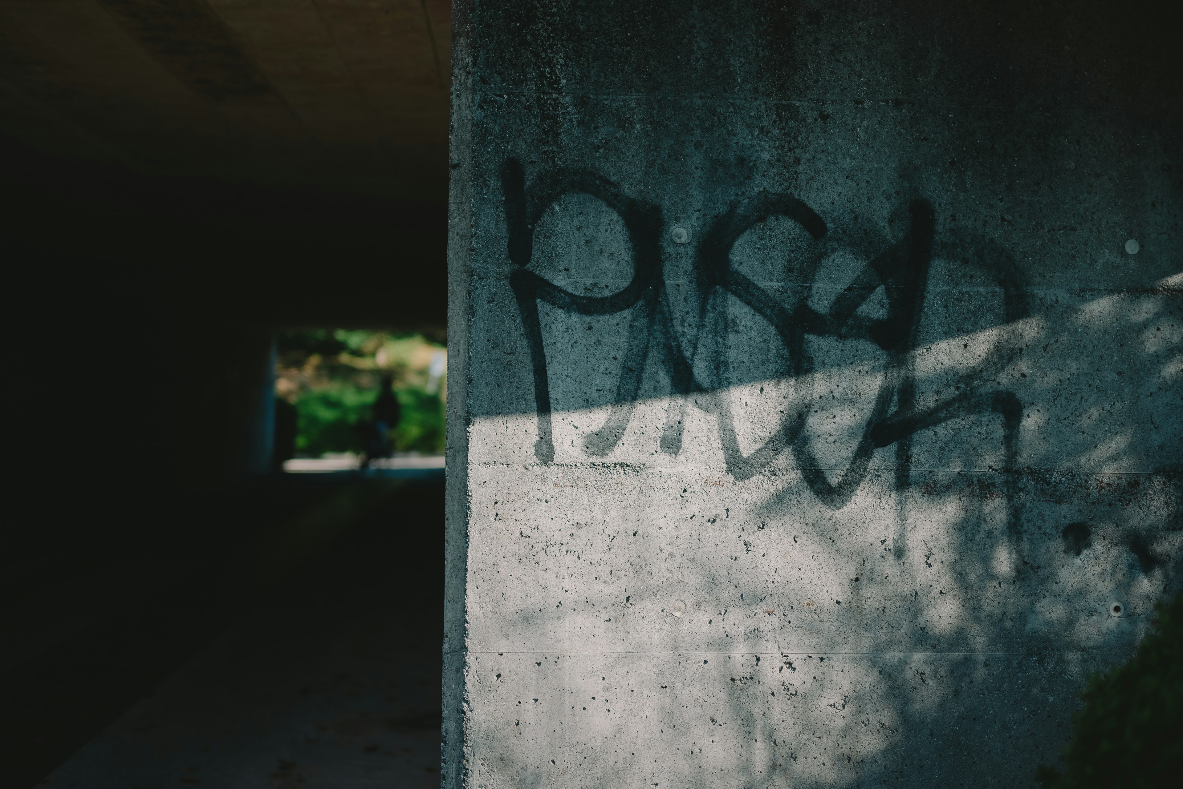 Graffiti su un muro di cemento con ombre e vista su un tunnel