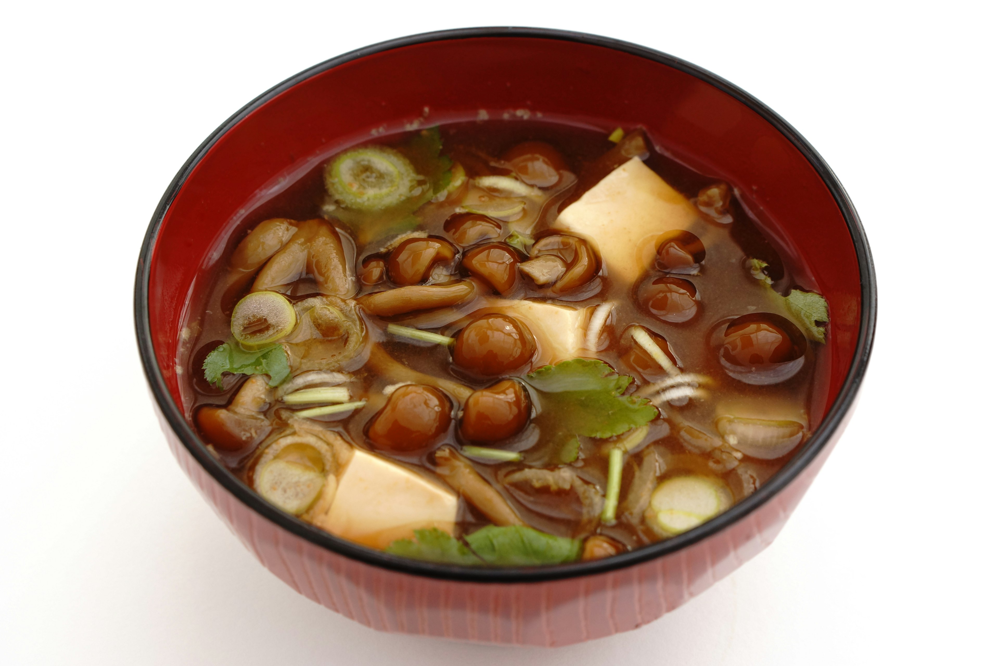 Miso soup in a red bowl with green onions tofu and mushrooms visible