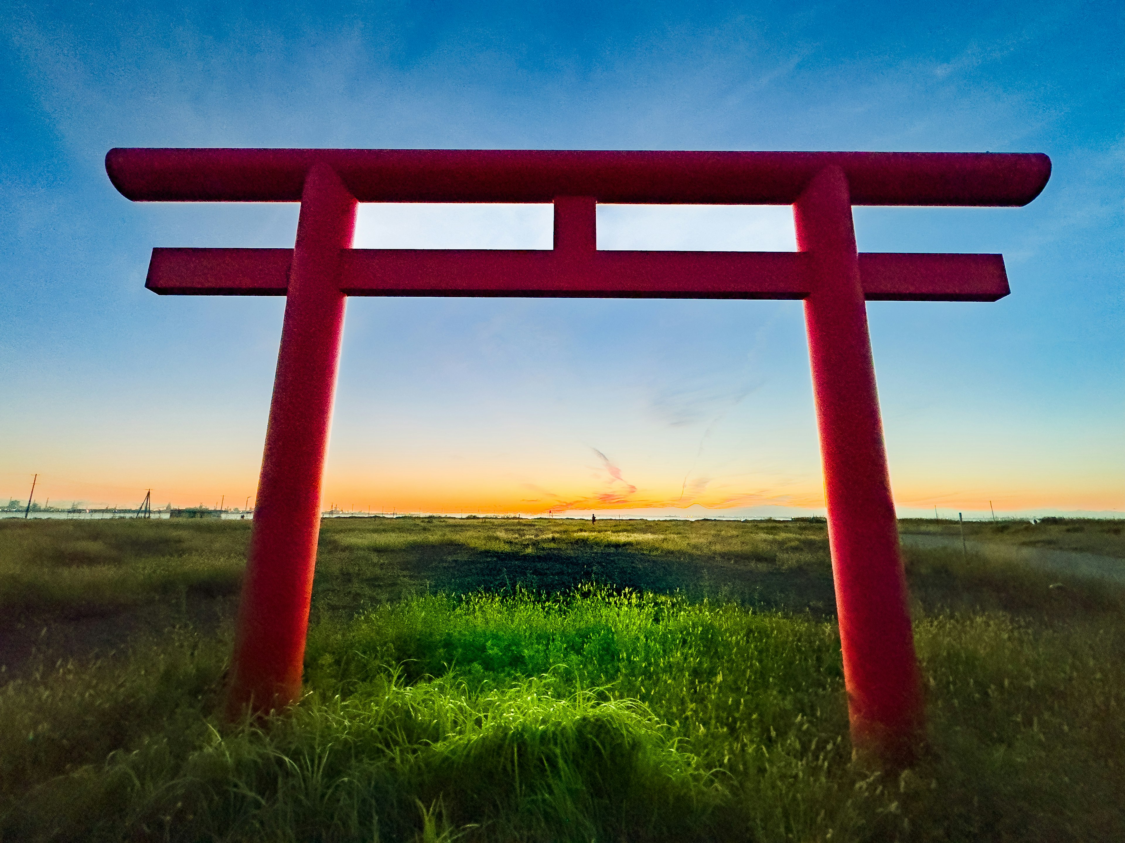 A red torii gate standing in a grassy field with a beautiful sunset in the background