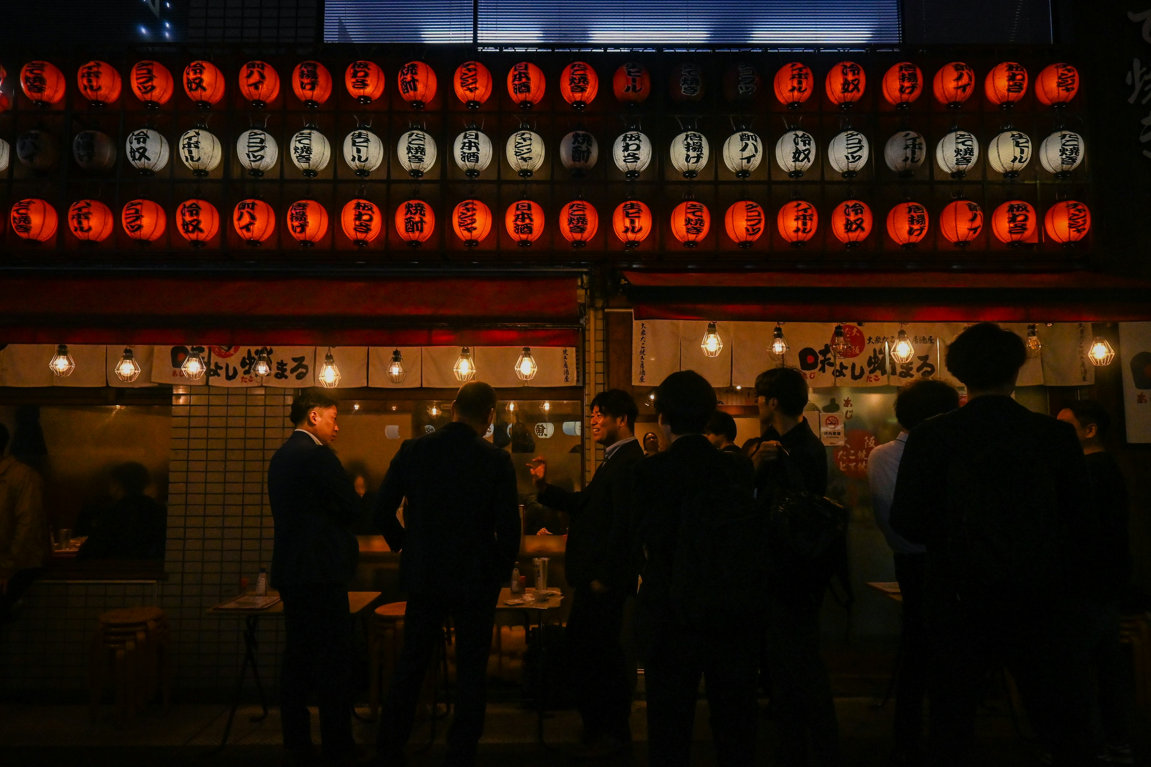 People gathered in front of a food stall at night with striking red lanterns