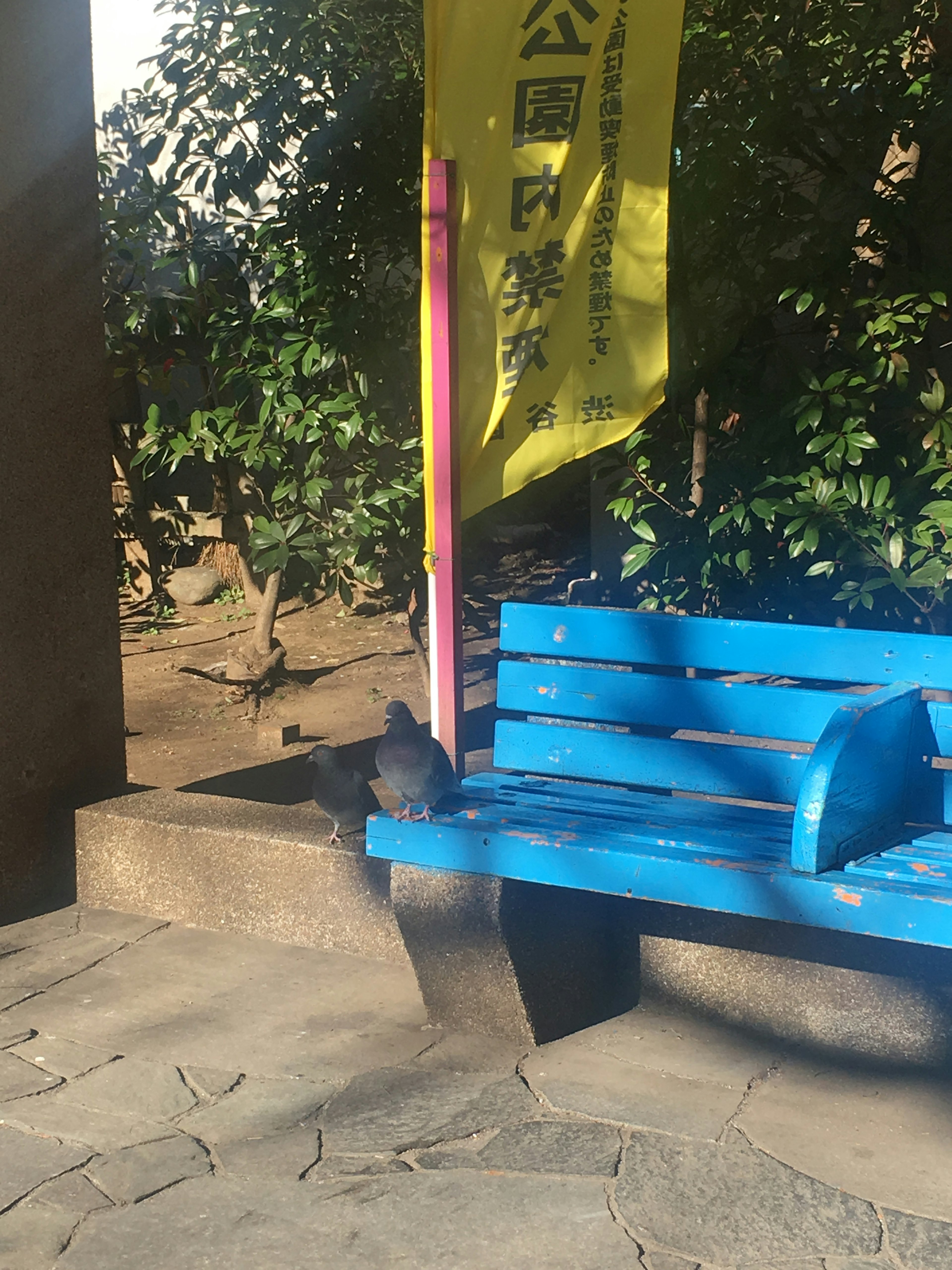 A blue bench with a yellow sign in a park setting