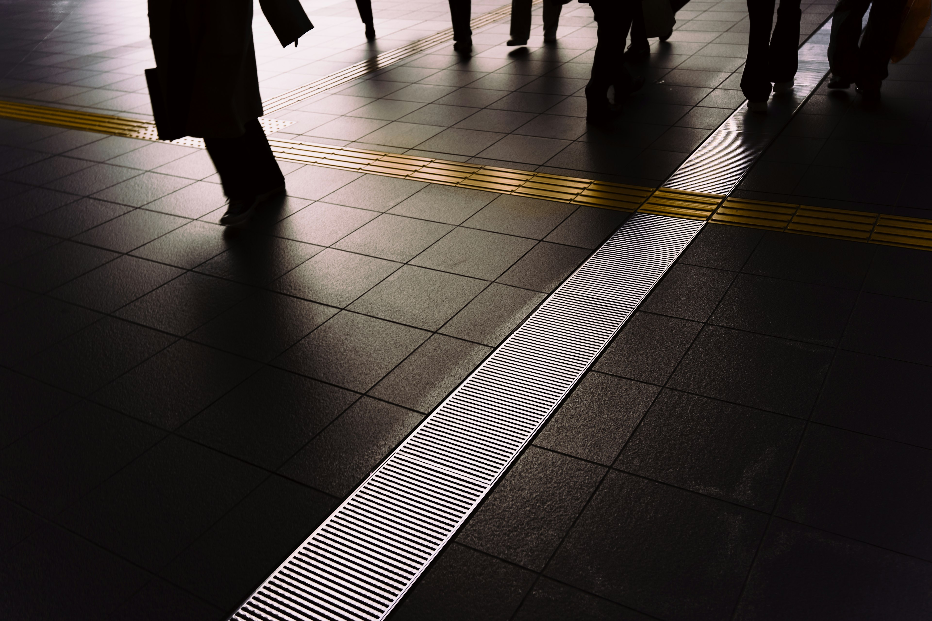 People walking on a station floor featuring a white guide line and a yellow line