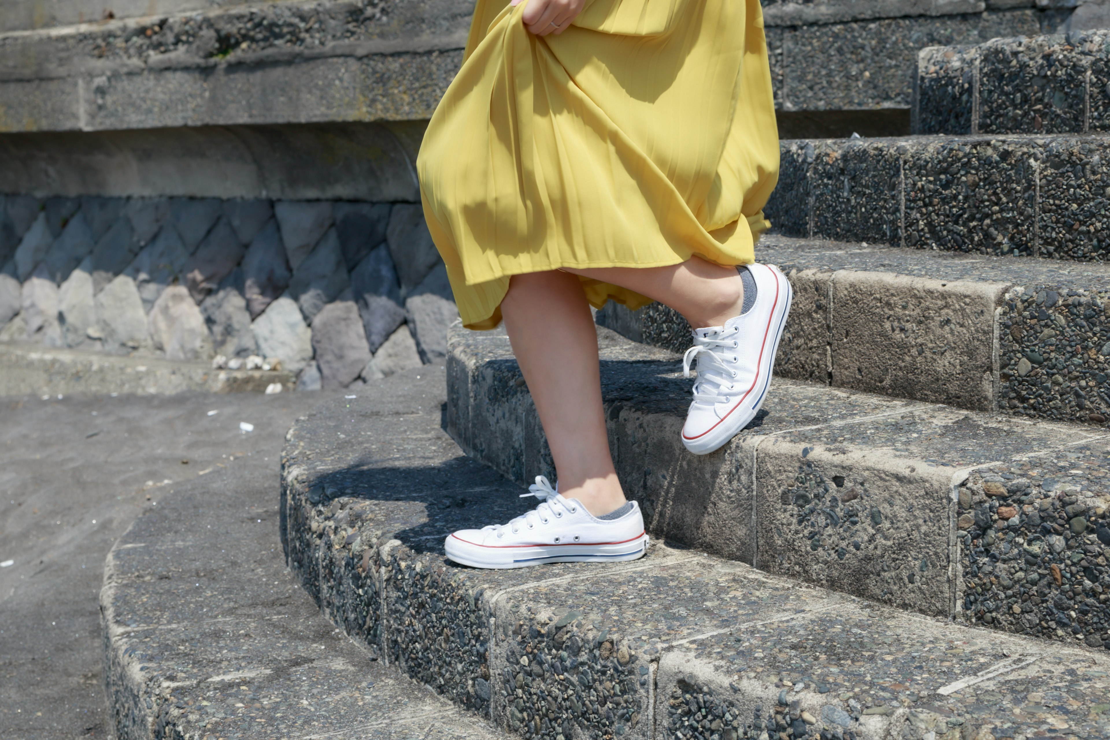 A woman in a yellow dress walking down stairs wearing white sneakers